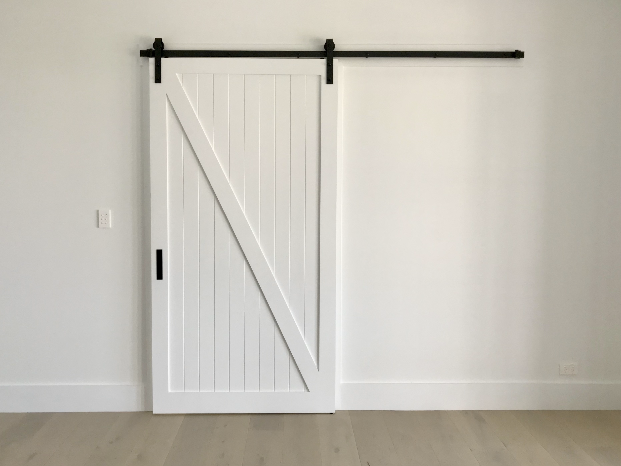 White sliding barn door with black hardware on a light-colored wall and light wood floor.