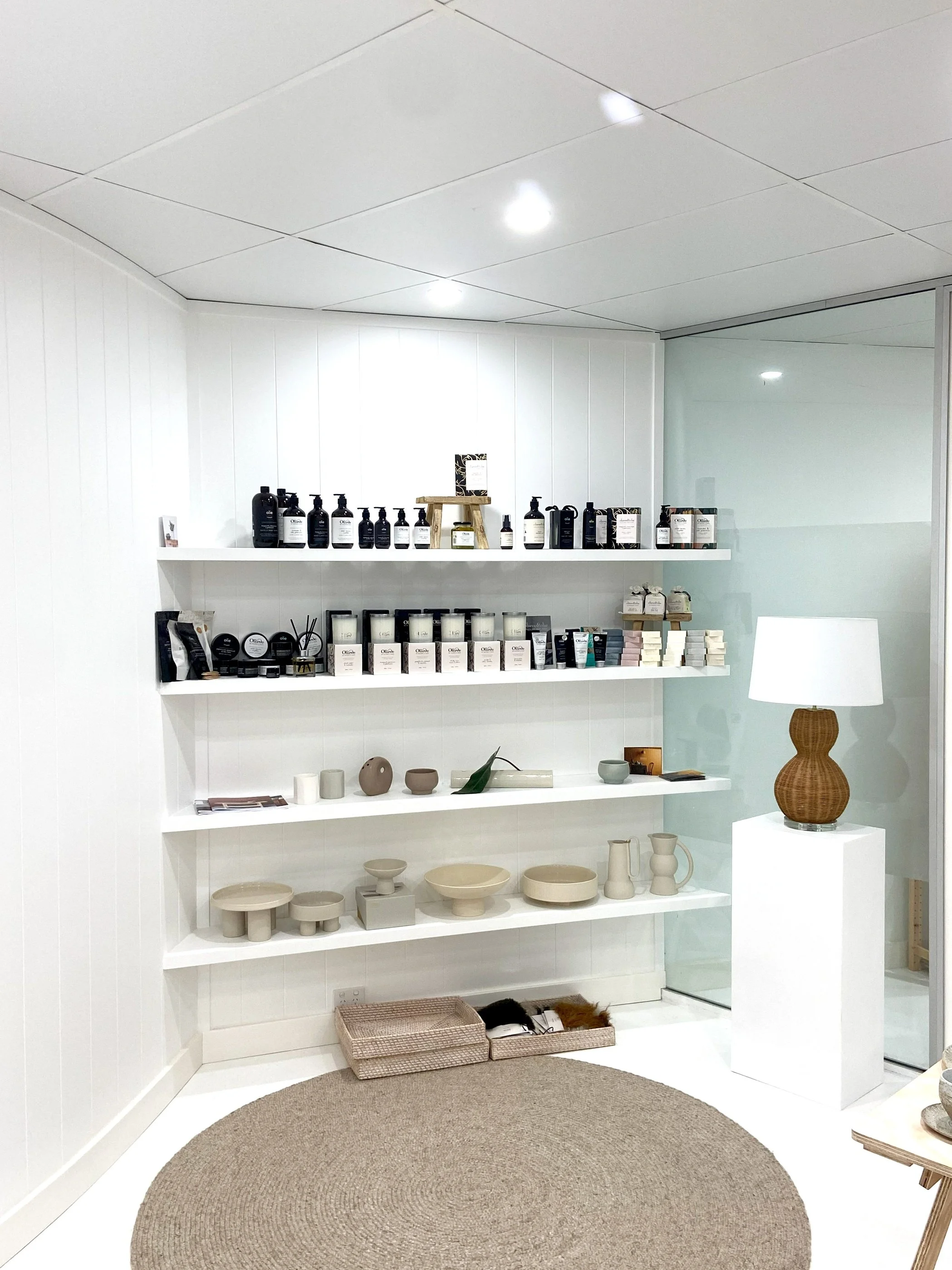 Display of skincare products, pottery, and home decor on white shelves in a minimalist store interior.