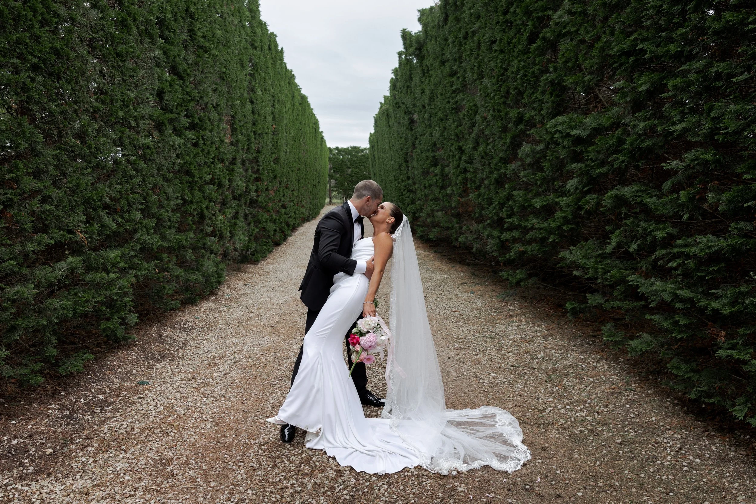 A bride and groom kiss on a road between two green hedges in Portsea, Melbourne.