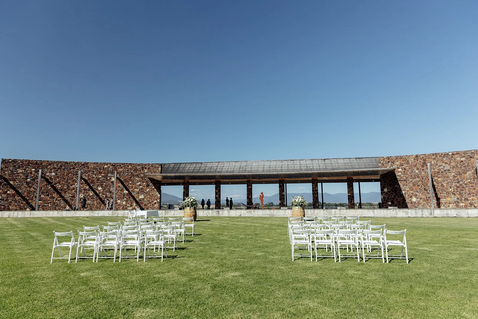 White chairs sit on a green lawn facing two wine barrels topped with flowers ready for the bride and groom's ceremony at Yering Station in the Yarra Valley.