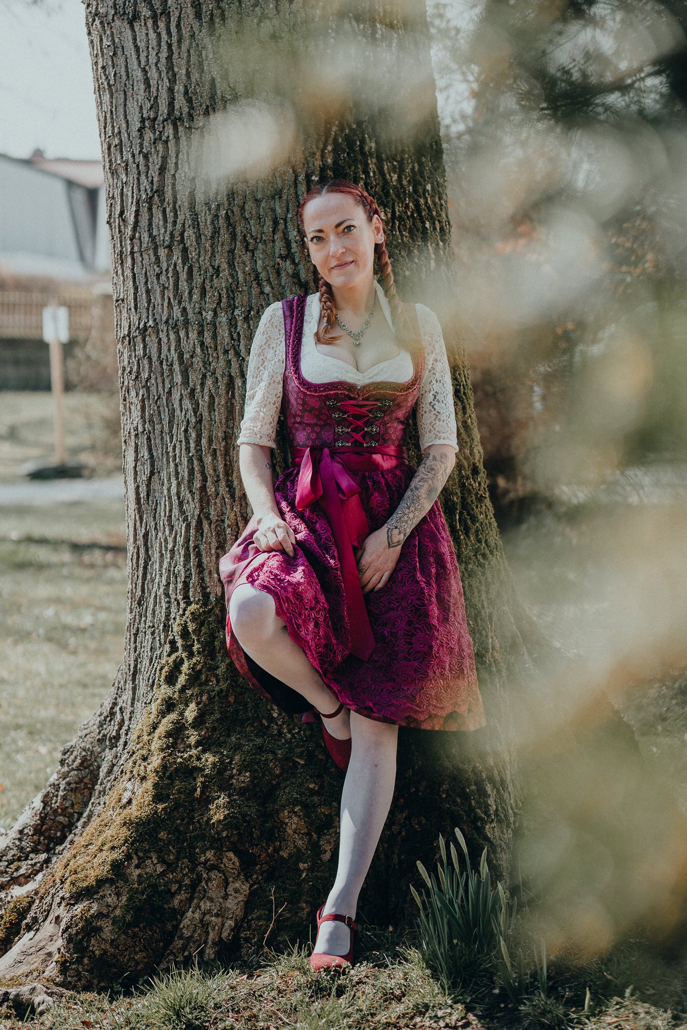 Frau in traditioneller bayerischer Dirndl steht an einem Baum im Freien.