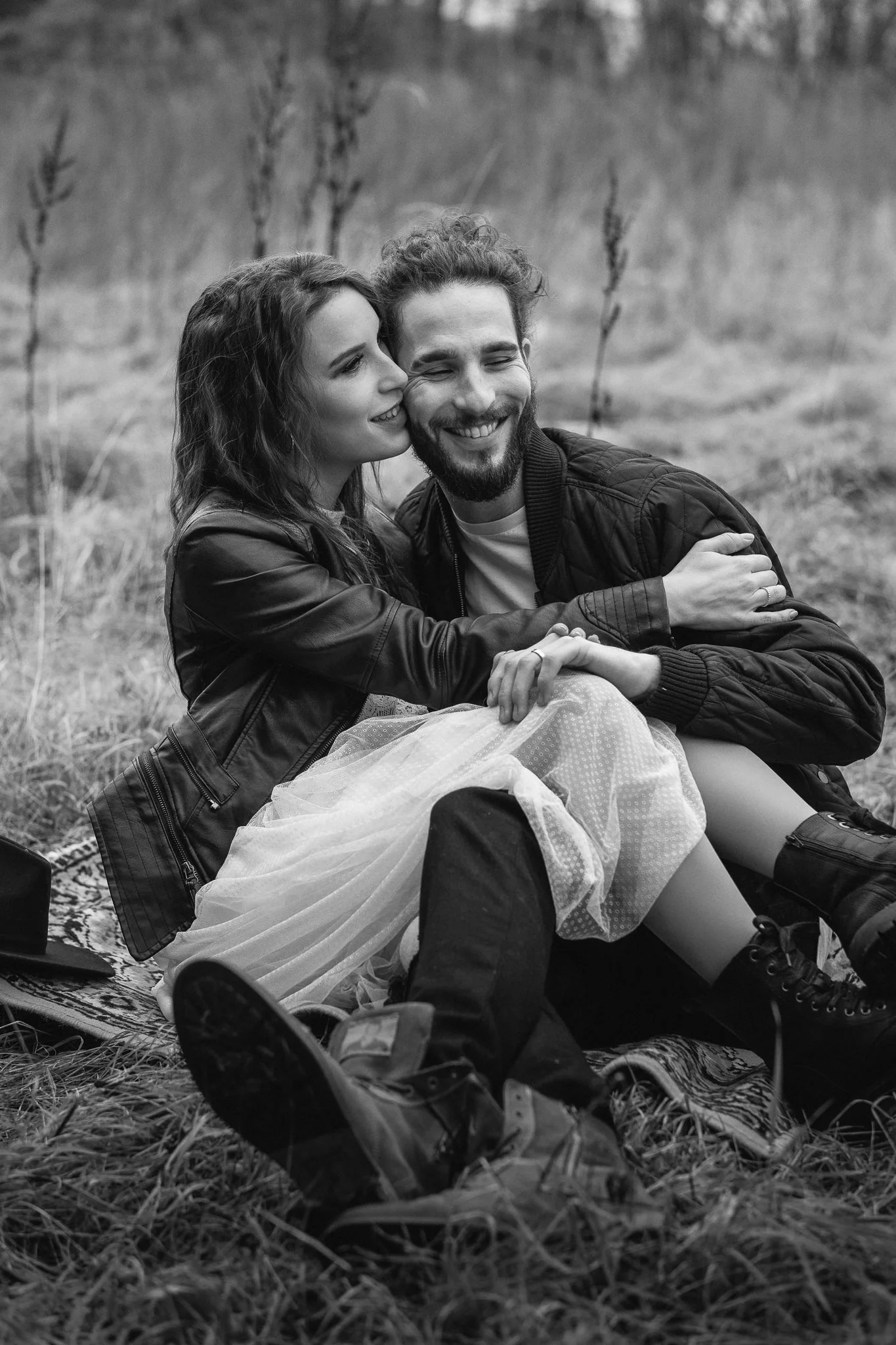 Ein glückliches Paar sitzt auf einer Decke im Freien, umarmt sich und lacht.