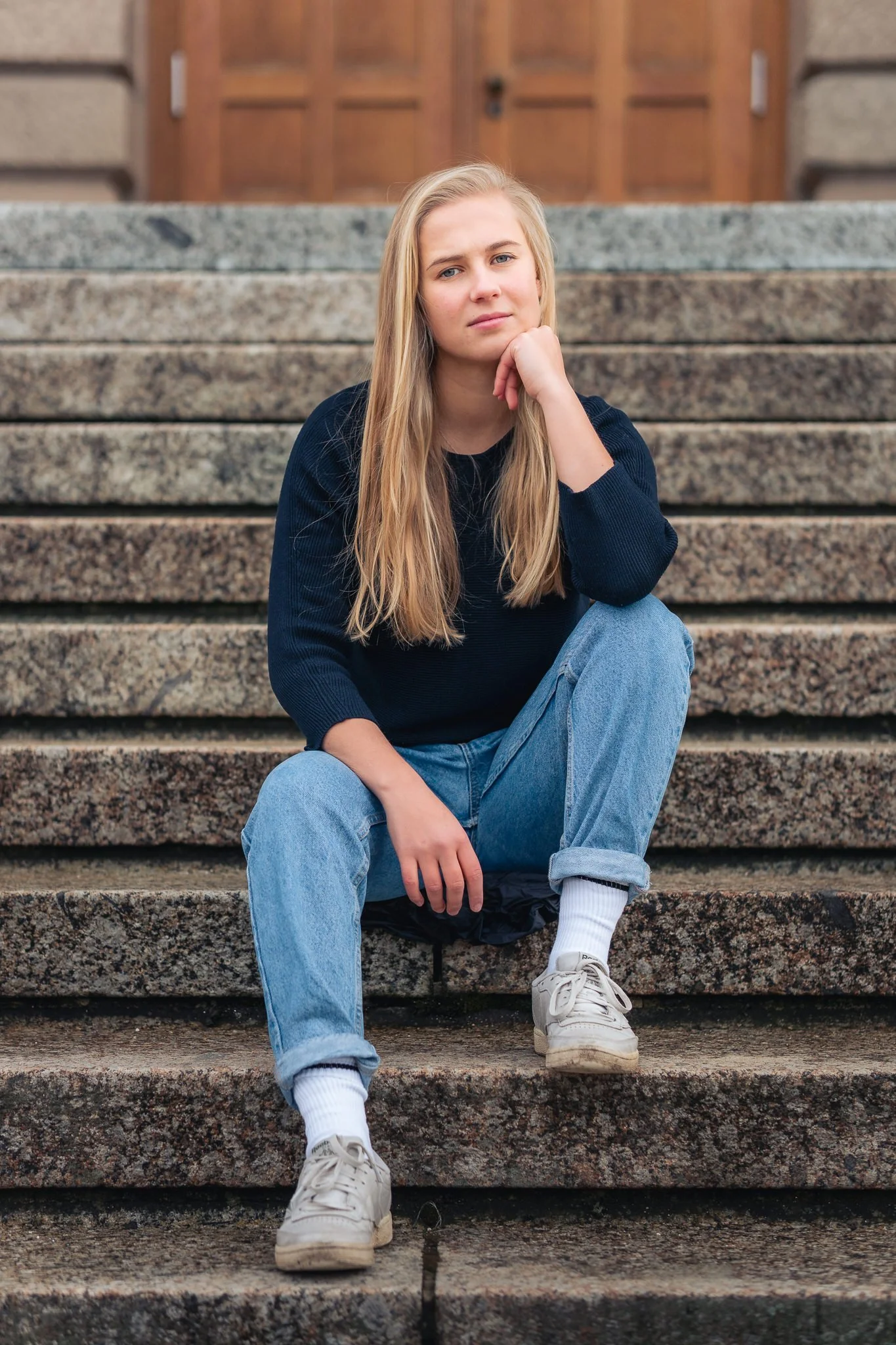 Junge Frau sitzt nachdenklich auf Steinstufen vor einem Holzportal.