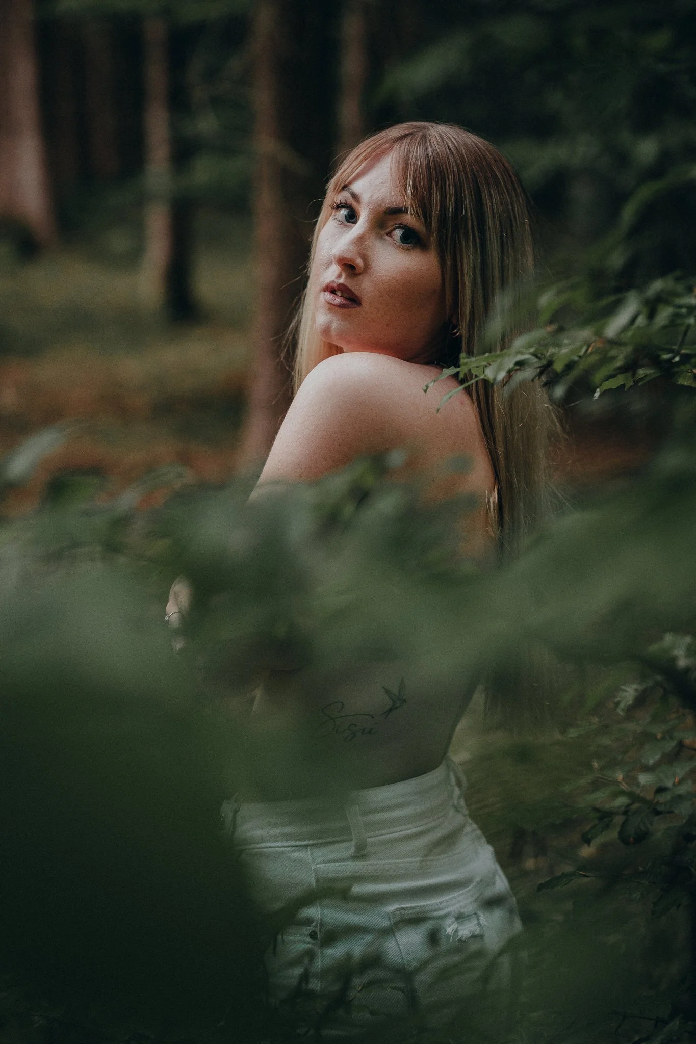 Junge Frau mit langem braunem Haar in einem Wald, umgeben von Blättern und Bäumen.