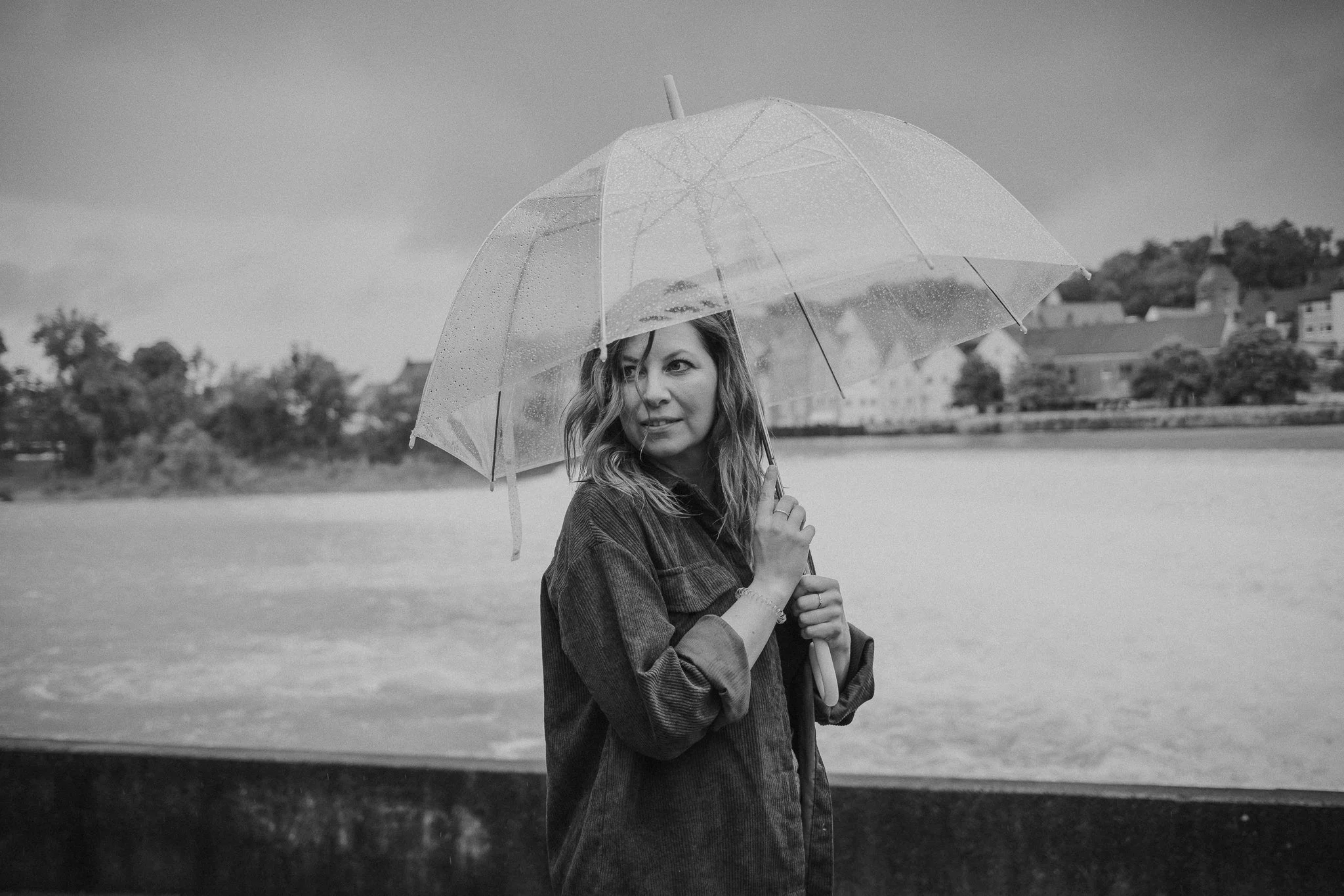 Frau mit Regenschirm am Flussufer bei Regen, schwarz-weiß