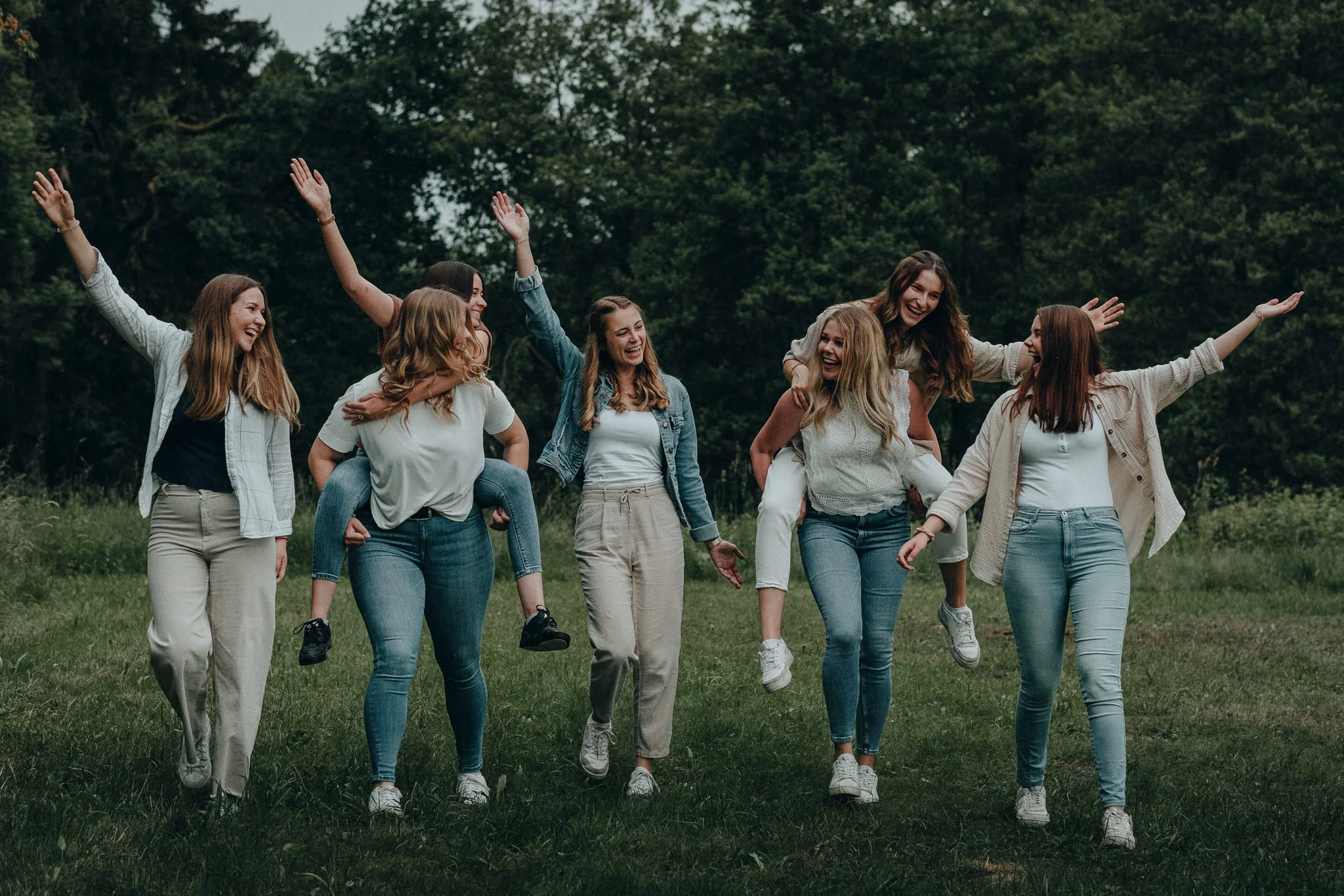 Sieben junge Frauen, die auf einer grünen Wiese im Freien lachen und Spaß haben