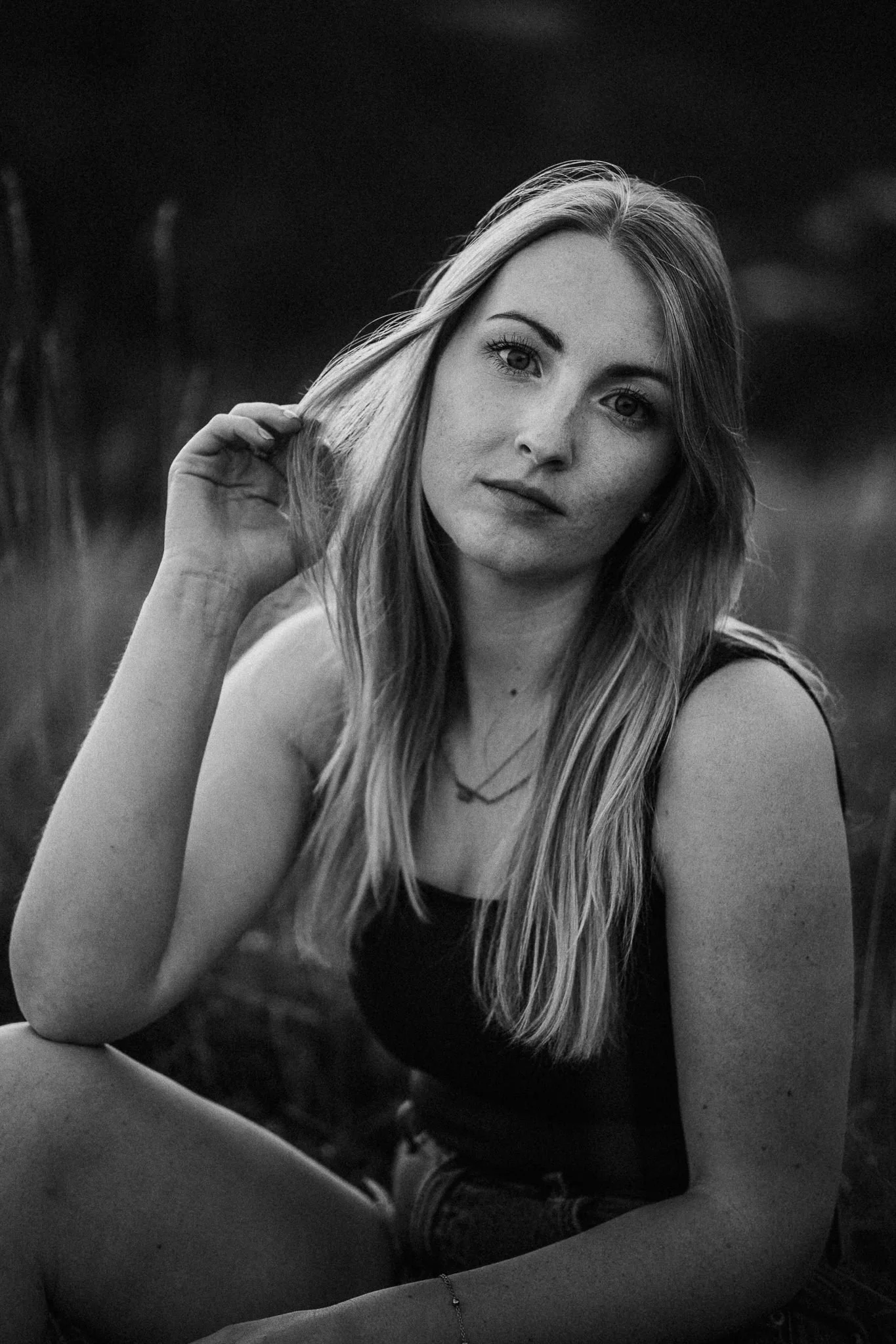 Porträt einer jungen Frau mit langen Haaren, die in einem natürlichen Umfeld im Freien sitzt.