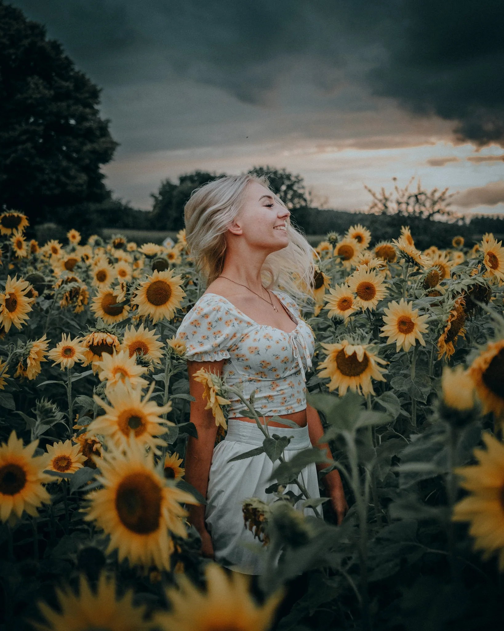 Eine lachende Frau in einem Sonnenblumenfeld bei Sonnenuntergang.