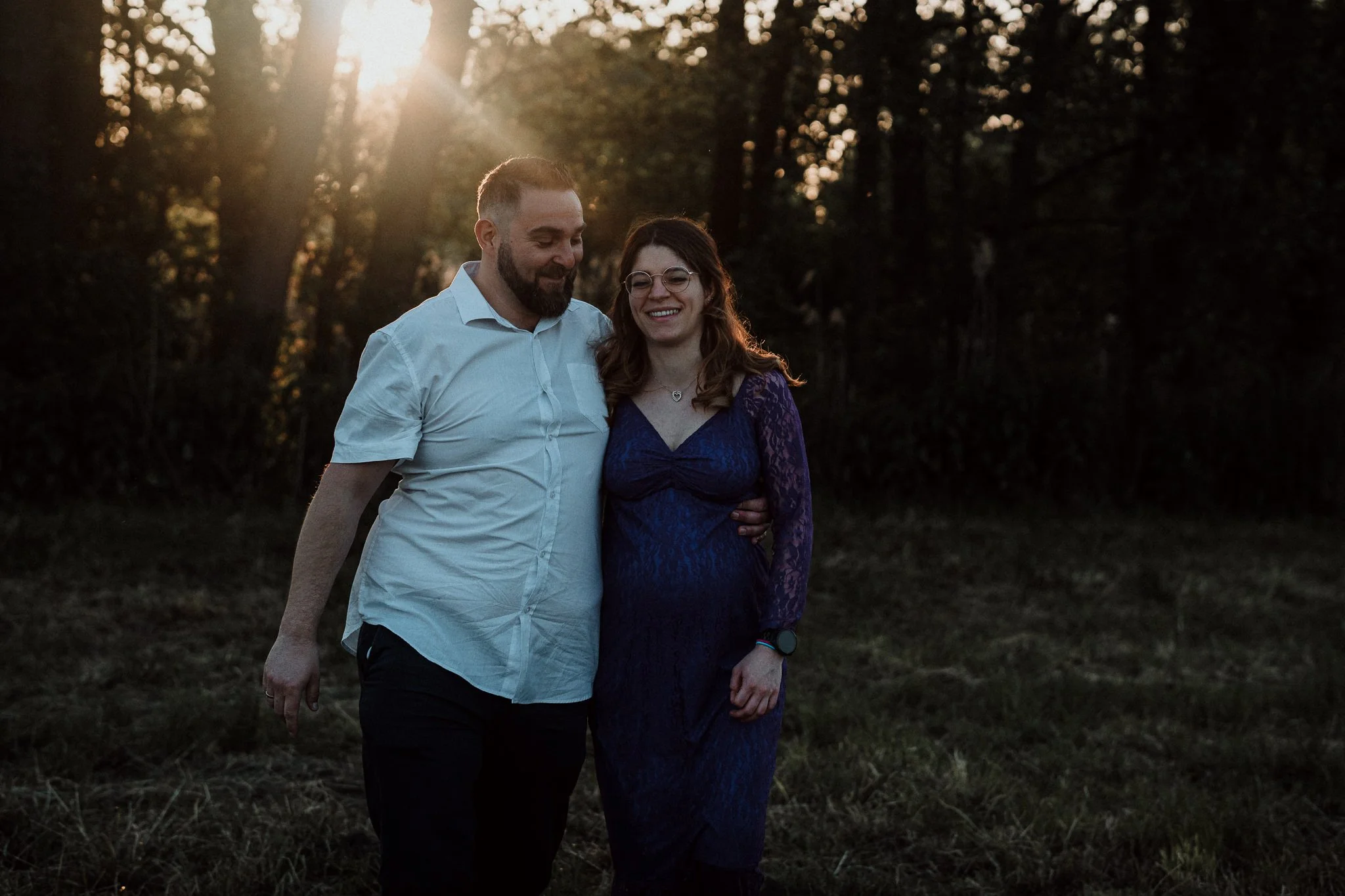 Ein Paar geht Hand in Hand durch einen Wald bei Sonnenuntergang, lächelnd und glücklich.