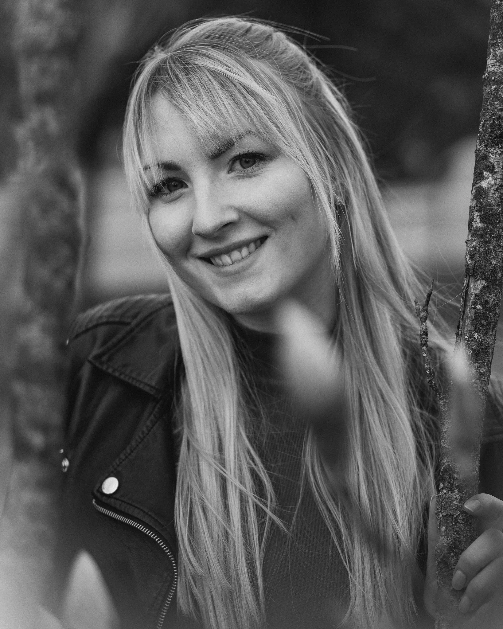 Schwarz-weiß-Fotografie eines lachenden jungen Mädchens, das in der Natur zwischen Bäumen steht.