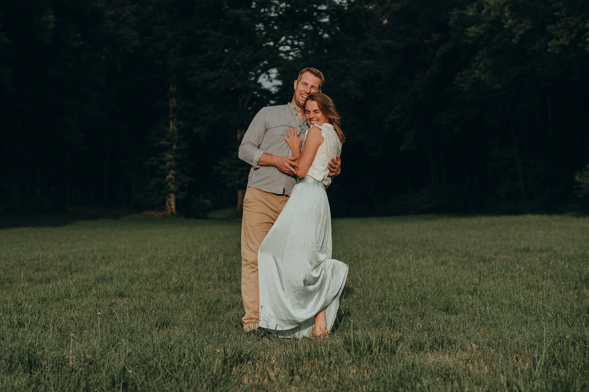 Ein glückliches Paar umarmt sich in einem offenen Feld mit Bäumen im Hintergrund.