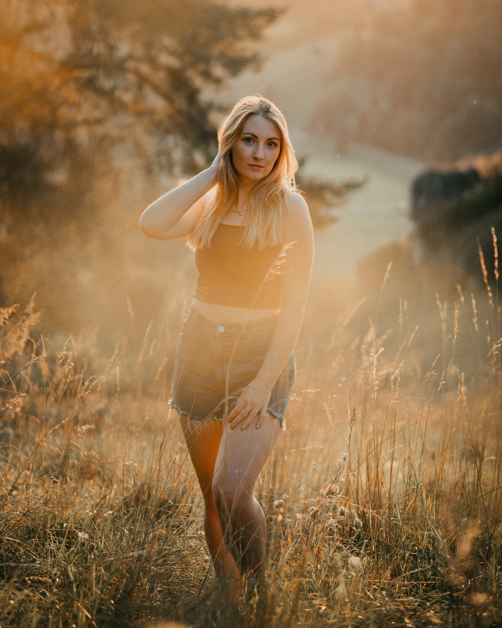 Junge Frau in einem Feld bei Sonnenuntergang, trägt schwarze ärmellose Top und Shorts, mit langem, blondem Haar.