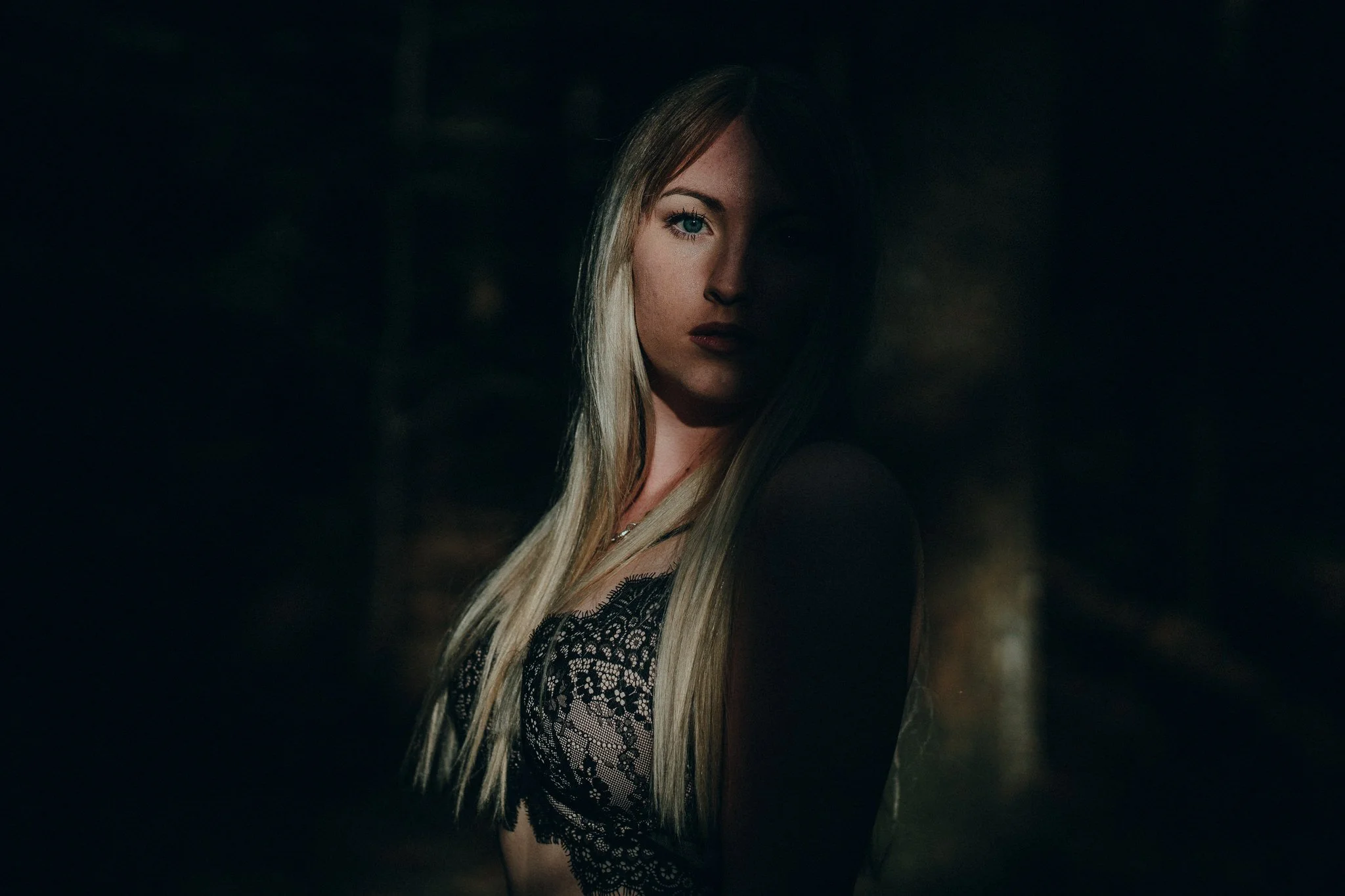 Porträt einer blonden Frau mit einem schwarzen Spitzenkleid, halb im Schatten in einer dunklen Umgebung.