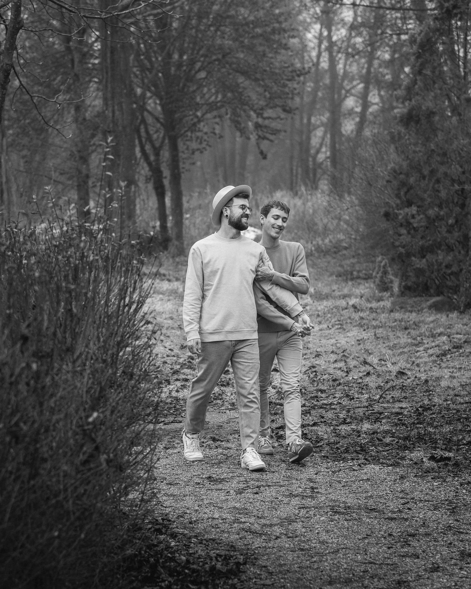 Zwei junge Männer spazieren in einem Wald, lachen und genießen die gemeinsame Zeit.