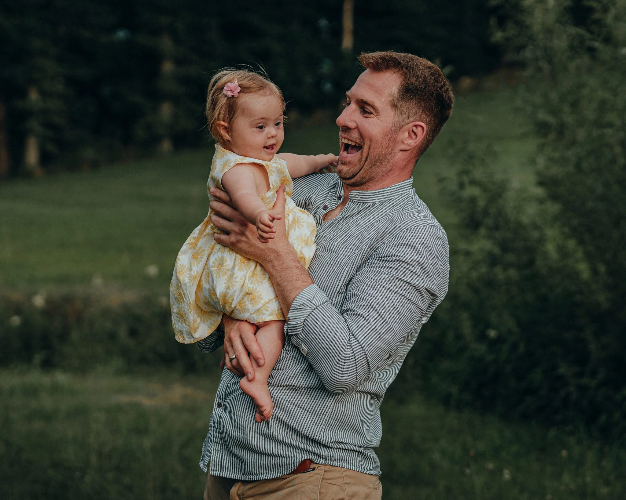 Ein Mann hält ein kleines Mädchen in einem grünen Park, beide lachen und freuen sich.
