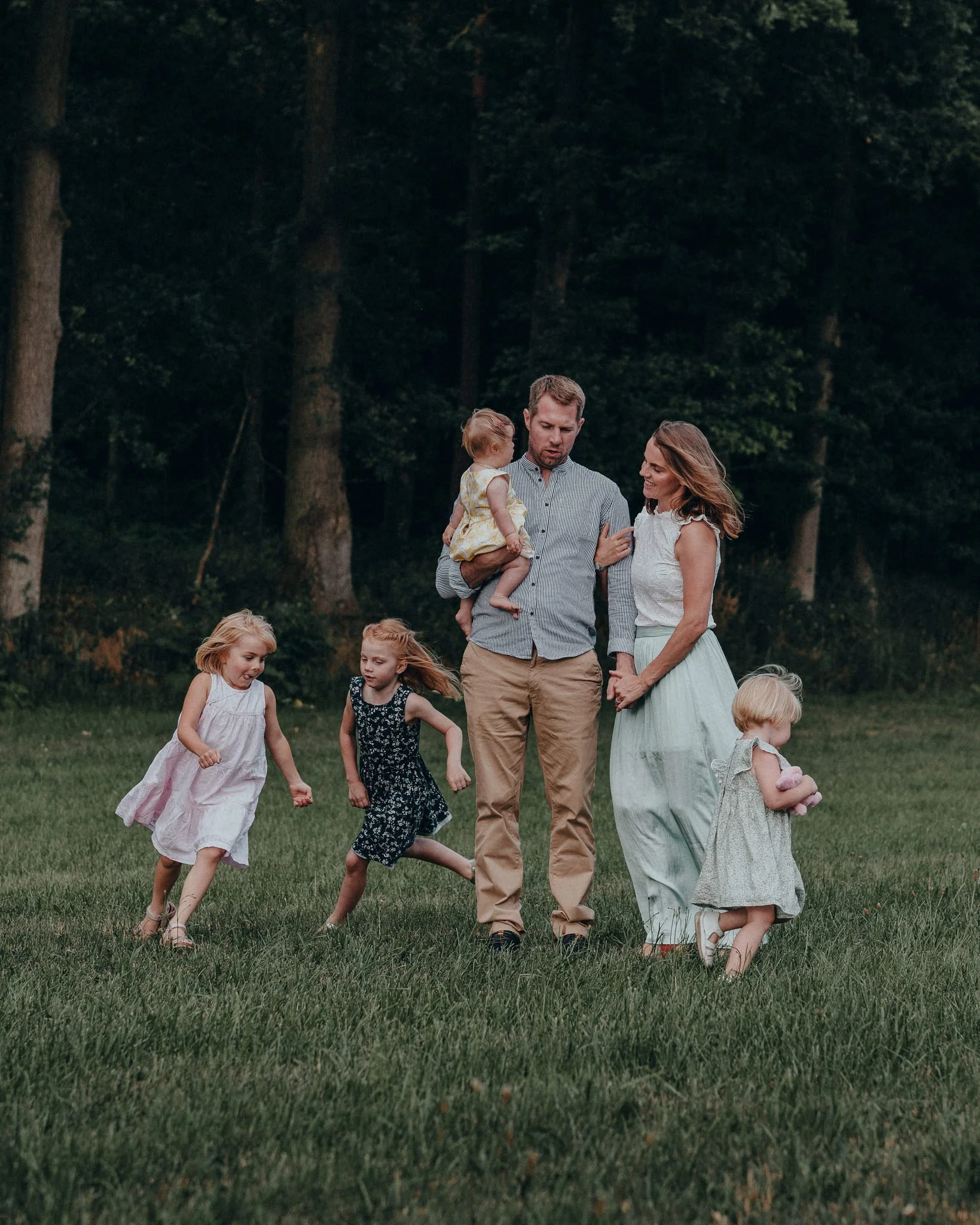 Familie mit Eltern und vier Kindern beim Spiel im Park auf dem Rasen, umgeben von Bäumen.