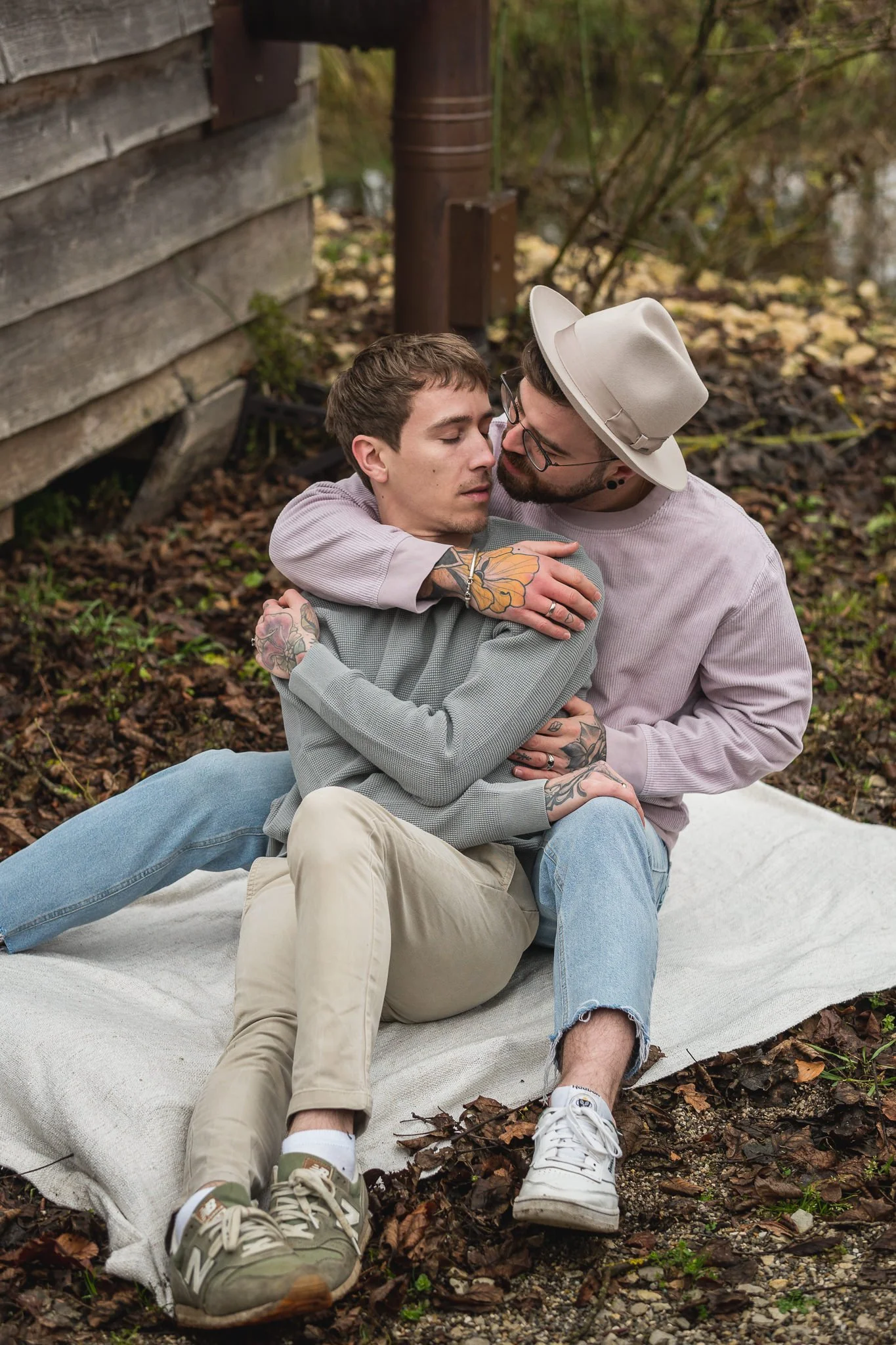 Zwei Männer in einer Umarmung auf einer Decke im Freien, umgeben von Laub im Herbst, eine romantische Szene.