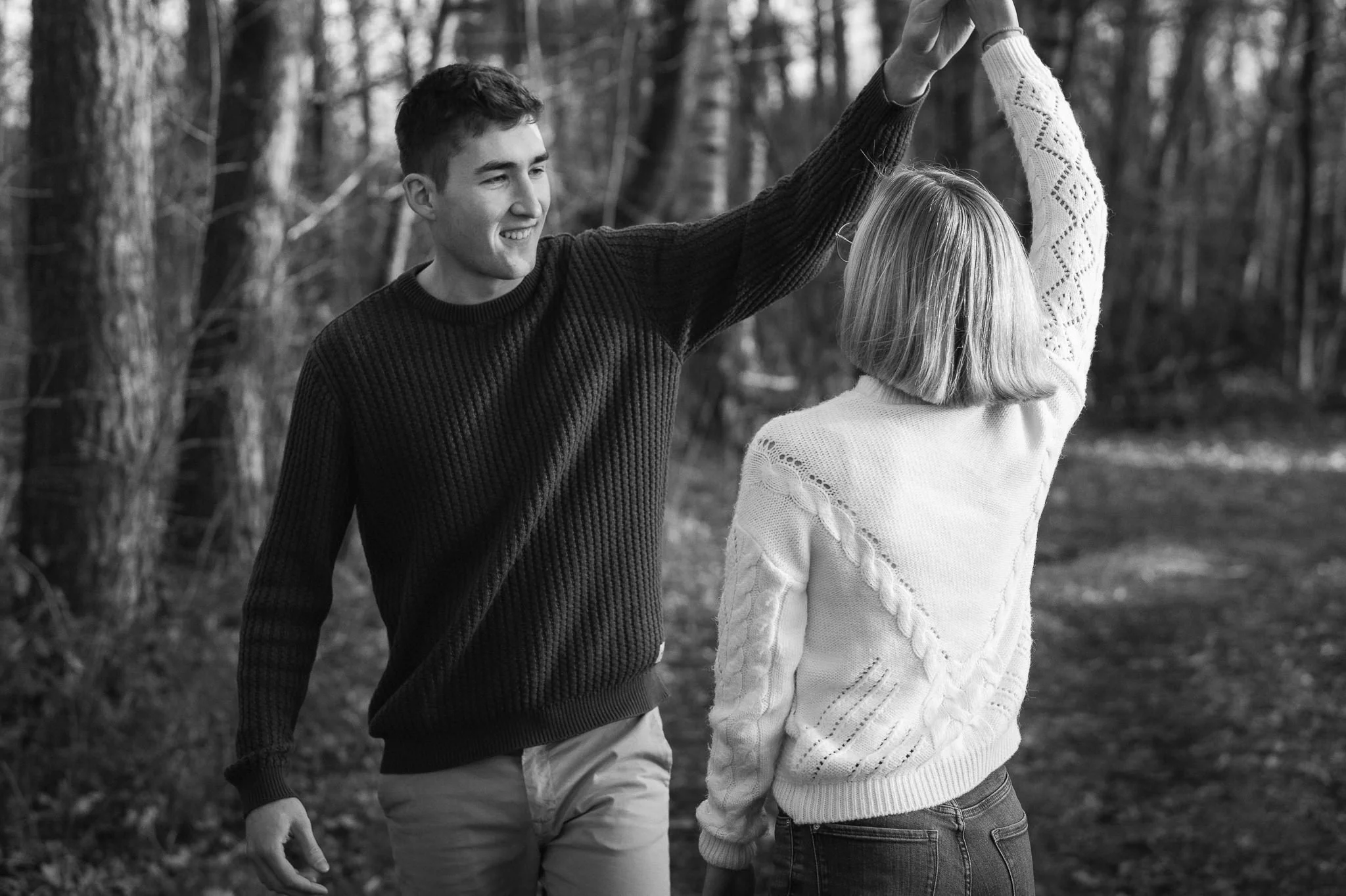 Ein Mann und eine Frau tanzen im Wald, der Mann hält die Hand der Frau hoch, sie lachen und haben Spaß.