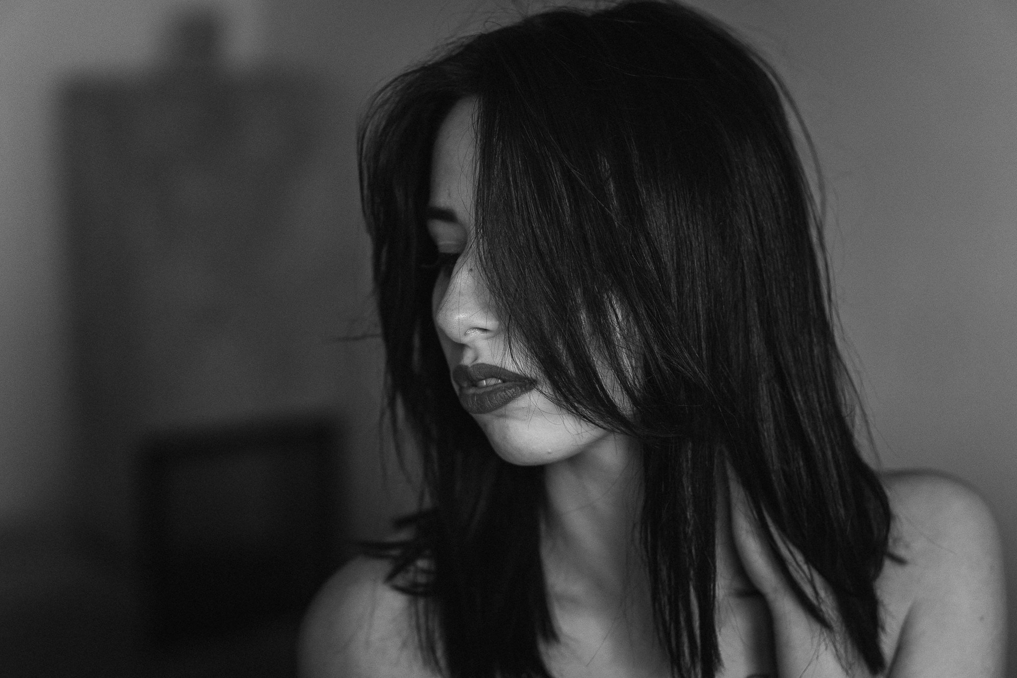 Schwarz-Weiß-Fotografie eines Mädchens mit dunklem, lockigem Haar, das teilweise das Gesicht verdeckt, und einem nachdenklichen Ausdruck, Blick nach unten.