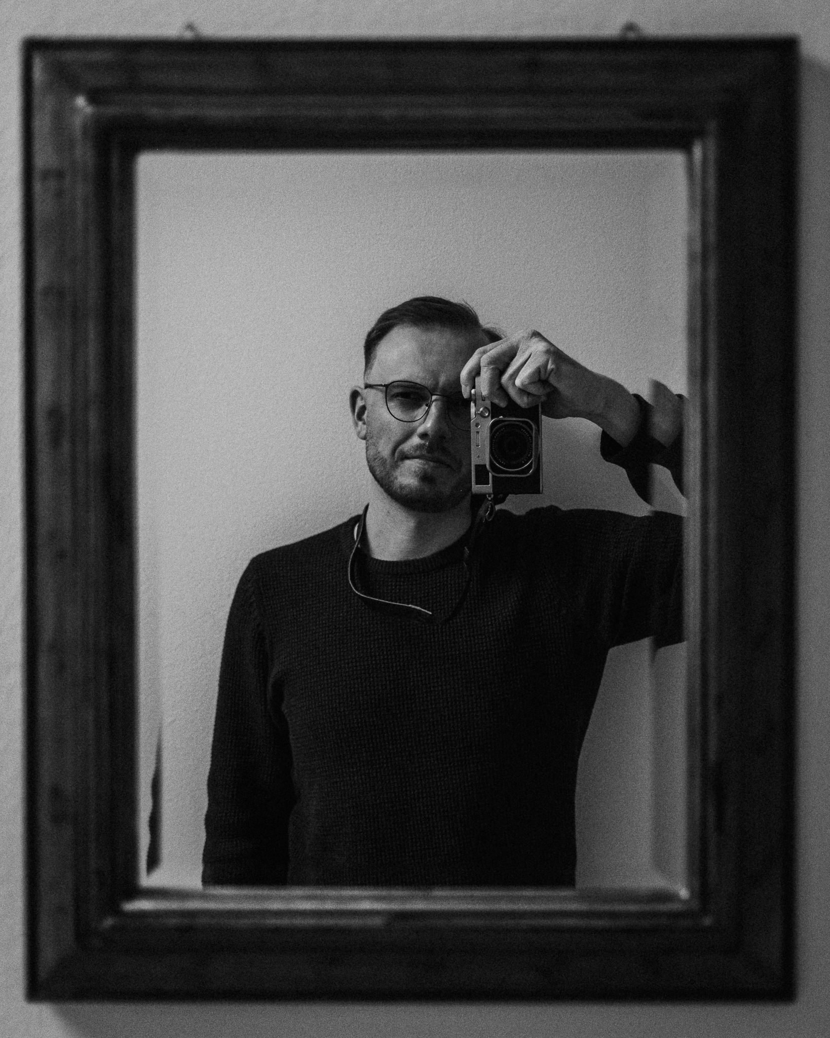 Mann macht Selbstporträt mit Kamera in Spiegel, schwarz-weiß, moderner Innenraum