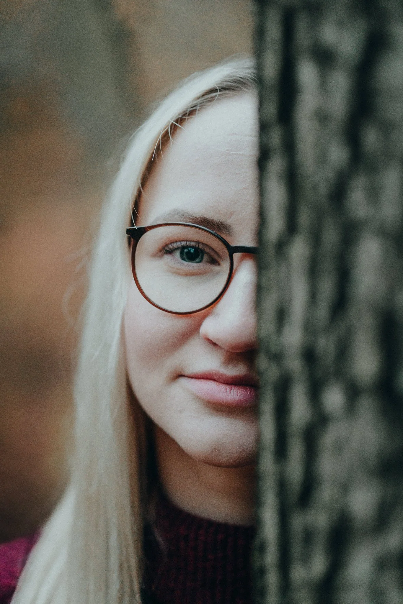 Nahaufnahme eines Mädchens mit Brille, halb hinter einem Baum versteckt, im Wald.