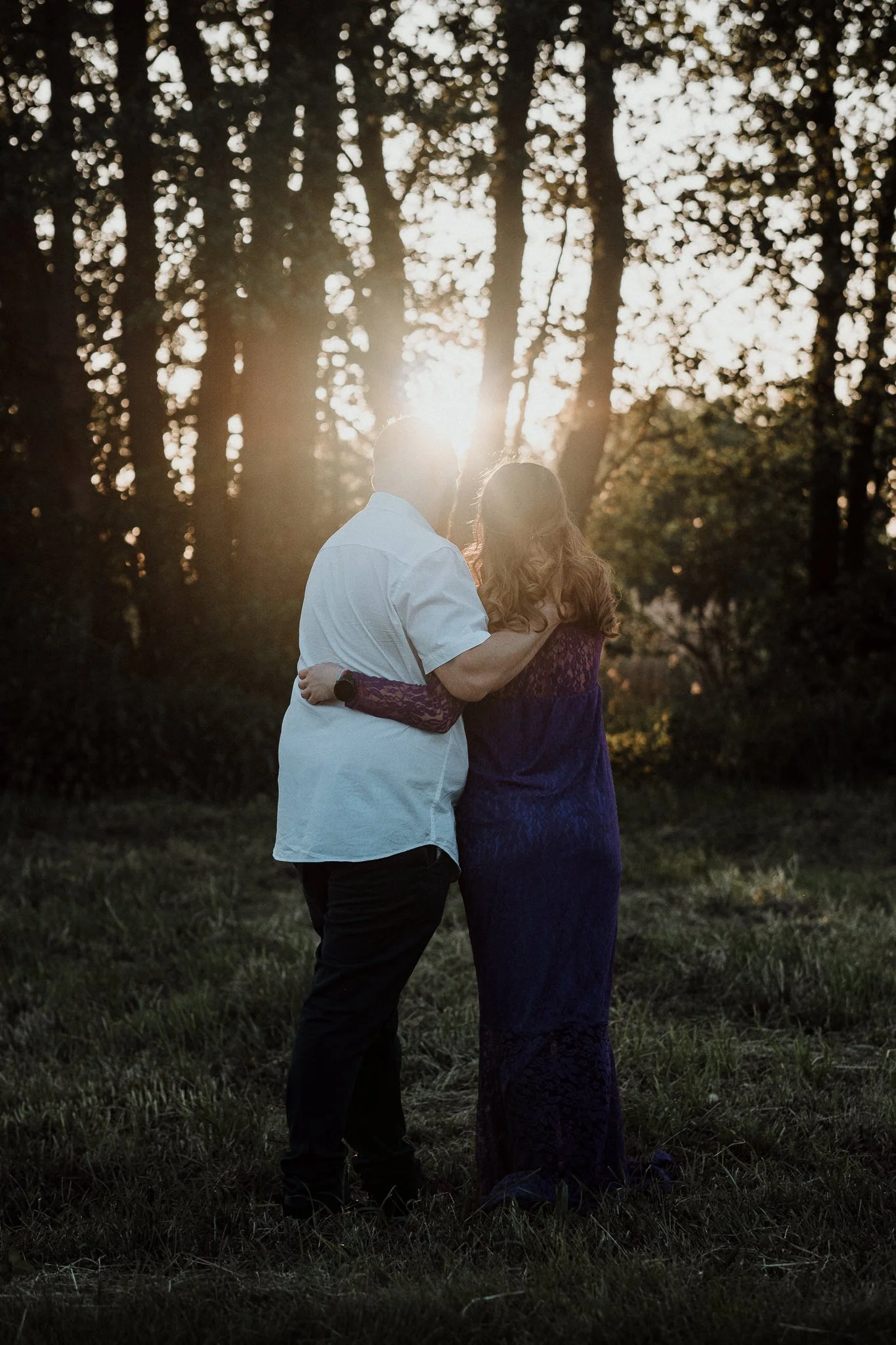 Ein Paar umarmt sich im Sonnenuntergang in einem Wald, Sonnenstrahlen scheinen durch die Bäume.