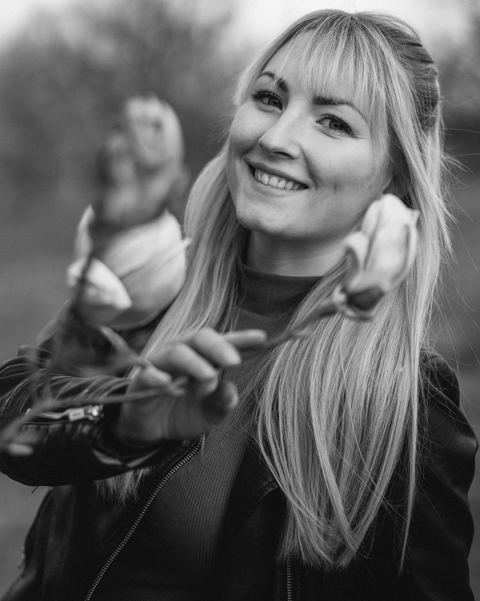 Schwarz-Weiß-Foto einer lachenden jungen Frau mit langen glatten Haaren, die eine Rose hält und nach vorne zeigt.