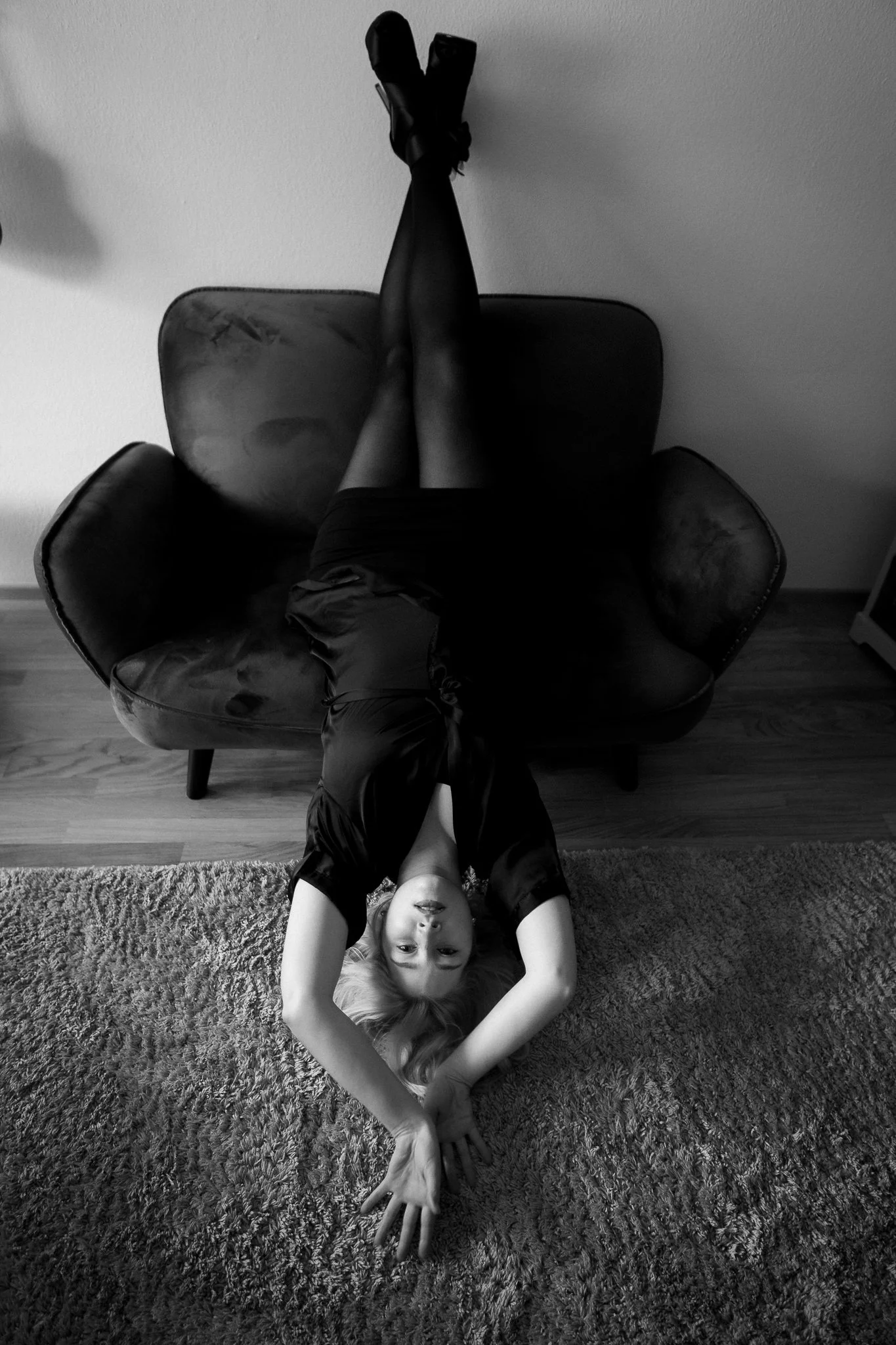 Schwarz-weiß-Foto eines Mädchens, das kopfüber auf einem modernen schwarzen Sessel liegt, mit Armen ausgestreckt nach vorne und Blick nach oben.
