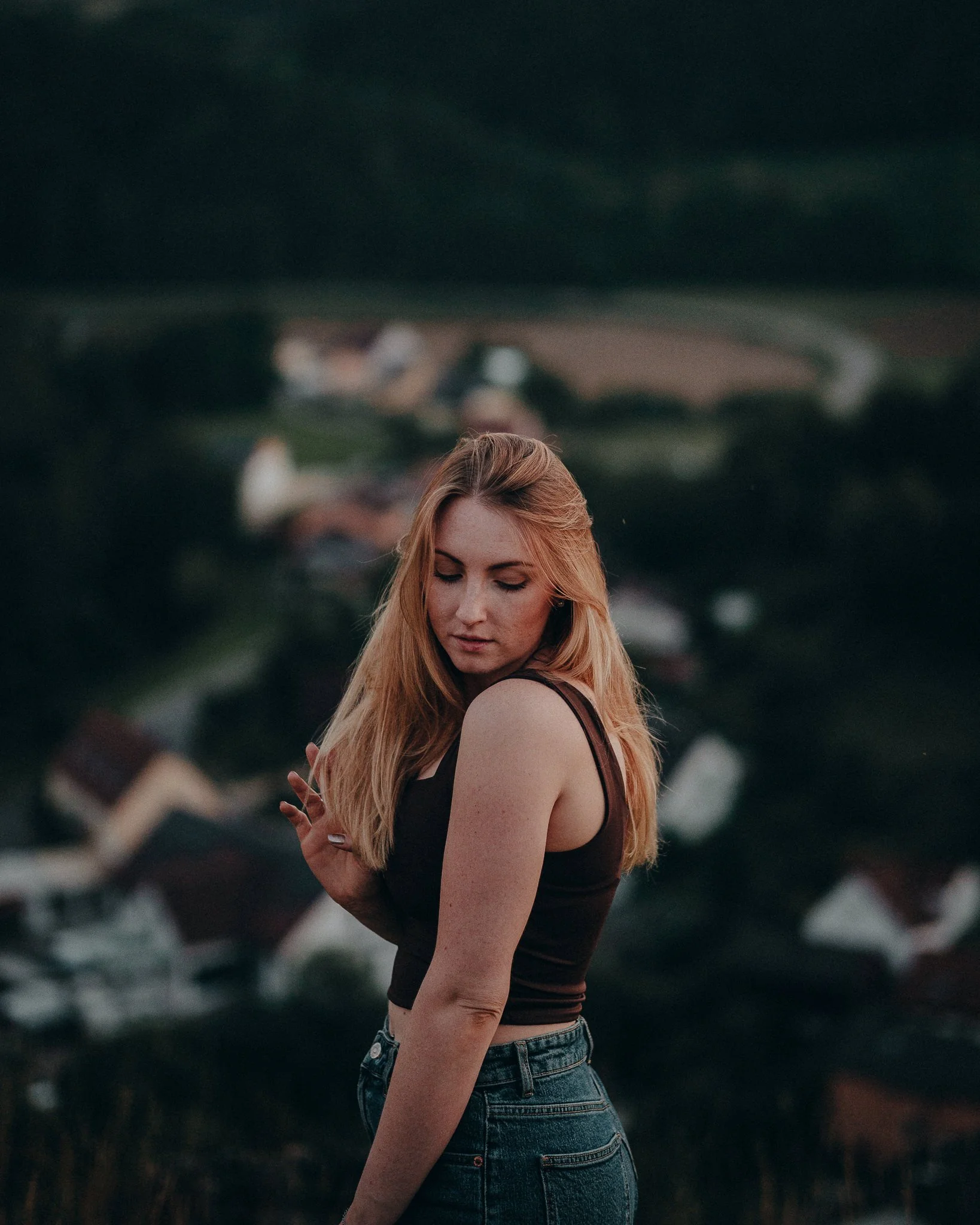 Ein junges Mädchen mit blonden Haaren posiert vor einer ländlichen Kulisse bei Sonnenuntergang.