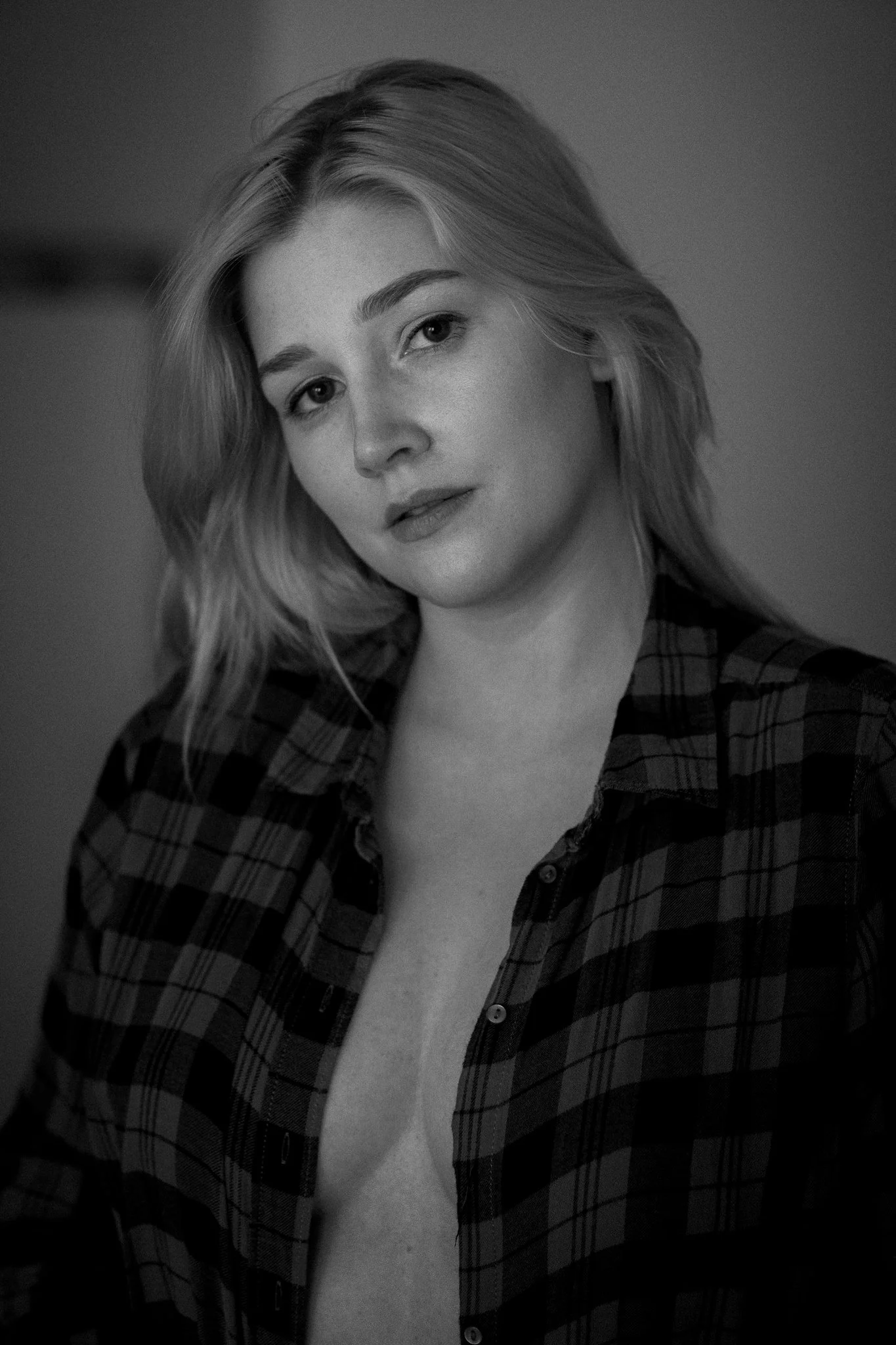 Schwarz-weiß Fotografie eines jungen Mädchens mit mittellangem, welligem Haar, das eine offene kariertes Hemd trägt.