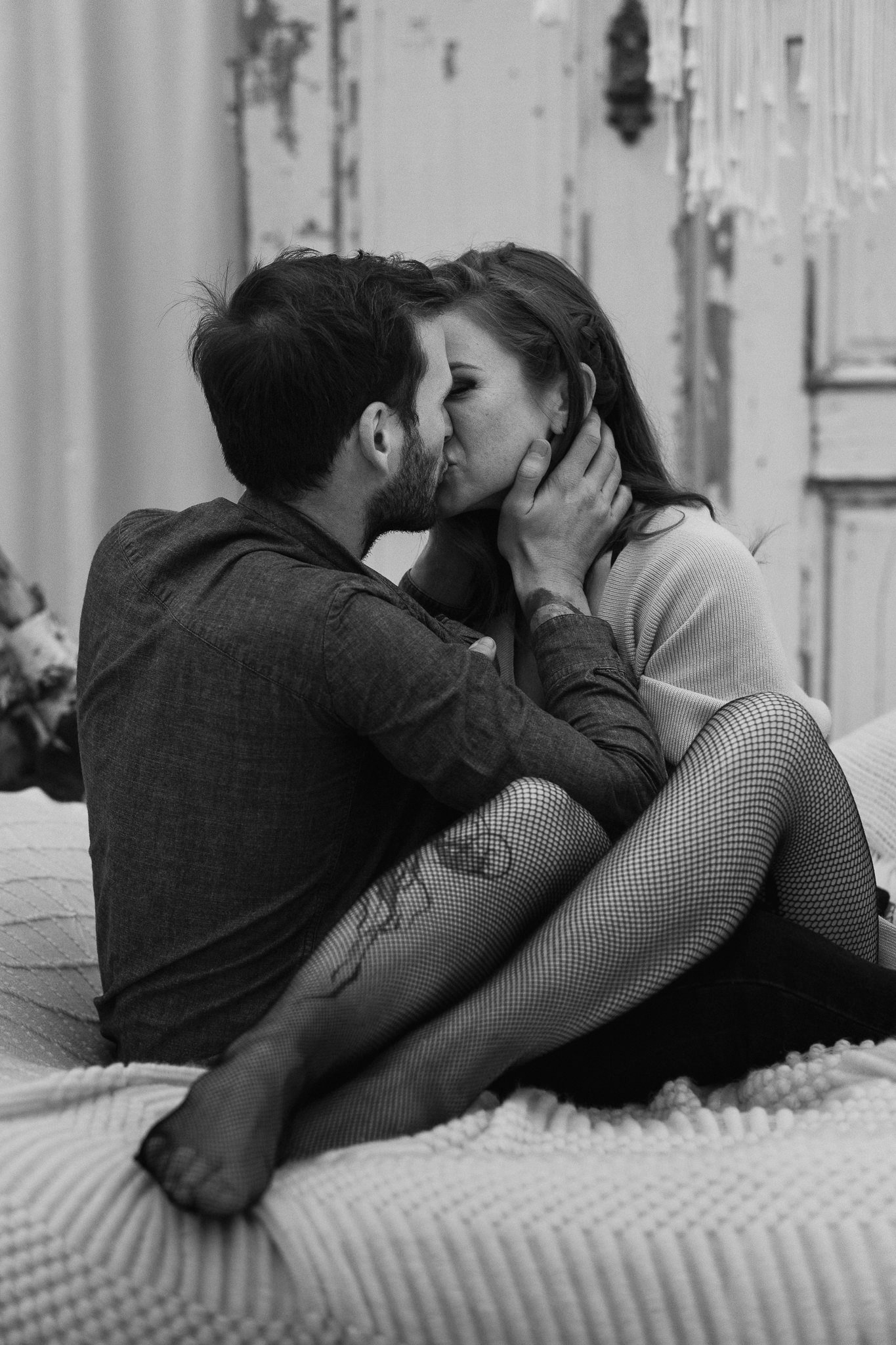 Ein romantisches Schwarz-Weiß-Foto eines Paares, das sich leidenschaftlich küsst, sitzend auf einem Bett mit Holzverzierungen im Hintergrund.