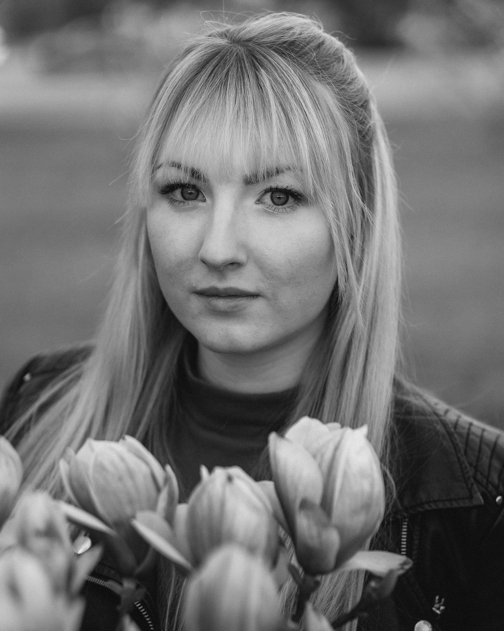 Schwarz-Weiß-Foto eines Mädchens mit langen Haaren, das vor einer Blumenwiese steht, Blick in die Kamera gerichtet.