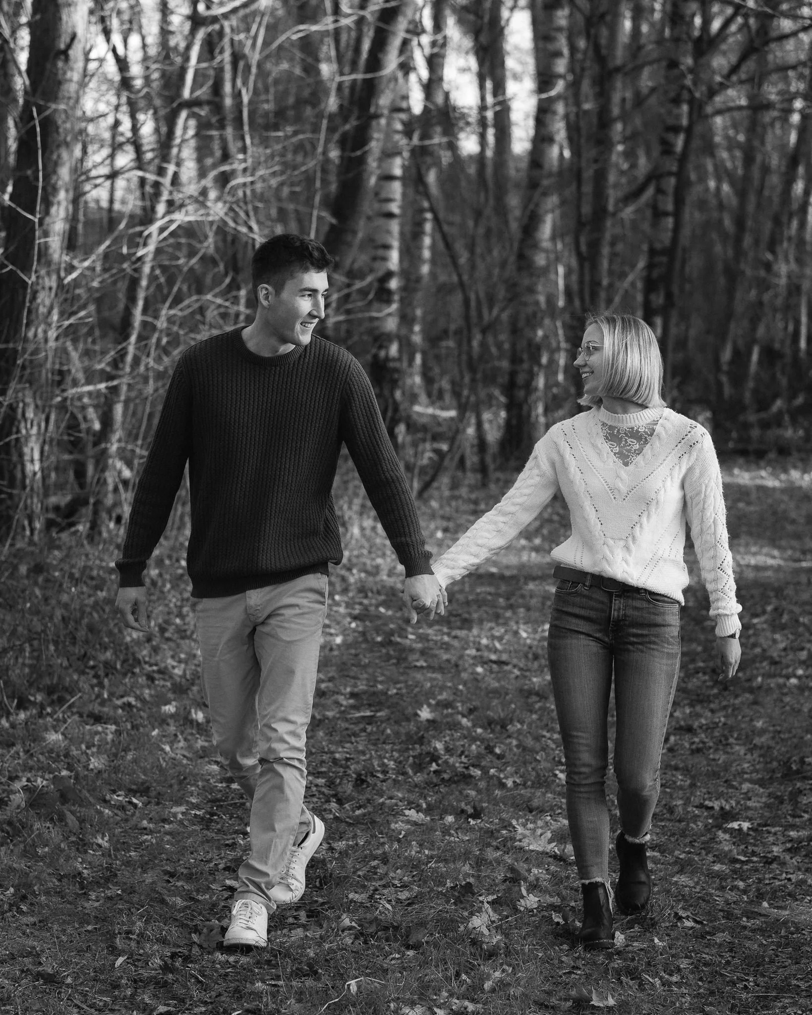 Ein junges Paar läuft Hand in Hand durch einen winterlichen Wald, beide lachen und wirken glücklich.