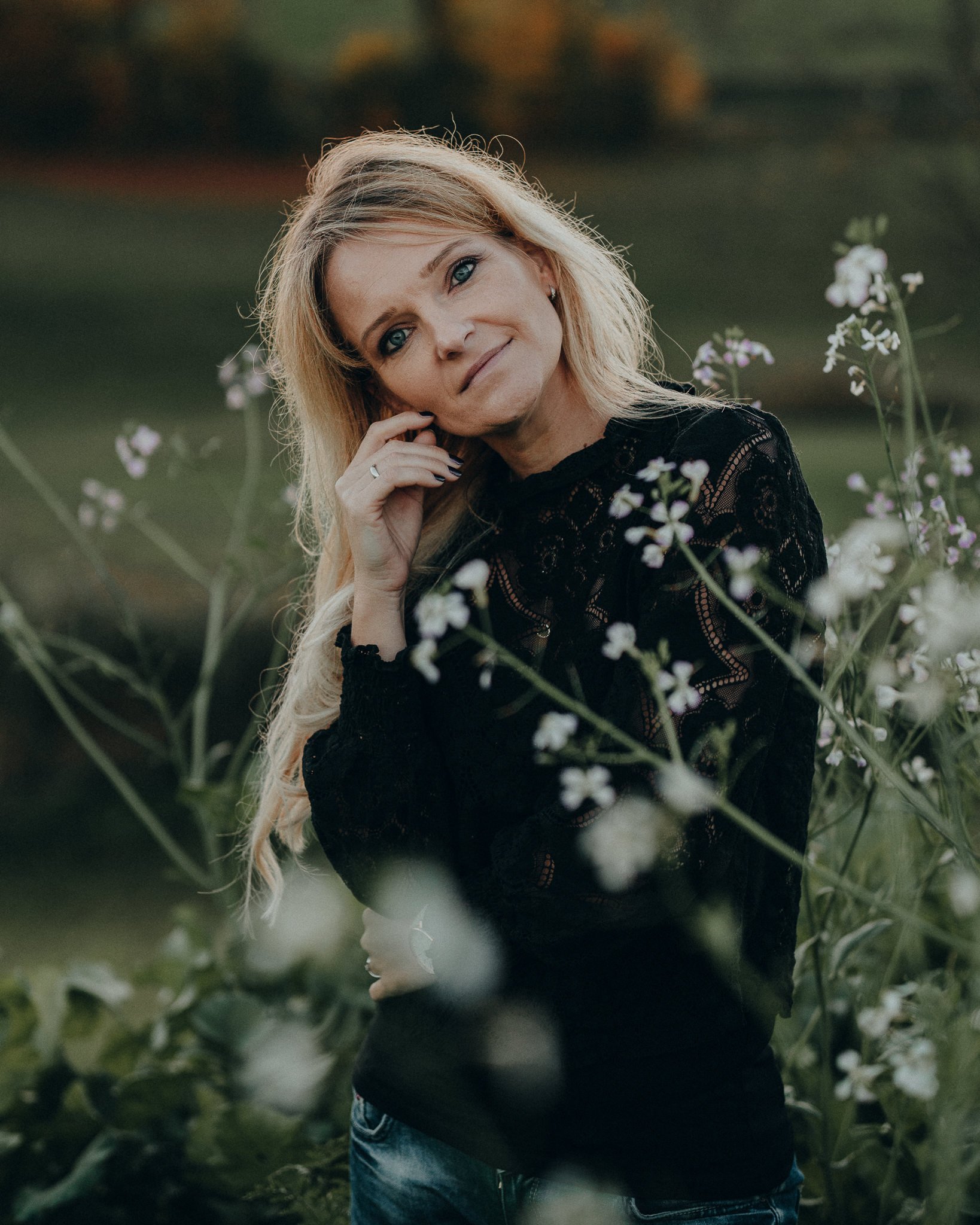 Frau mit blonden Haaren in einer schwarzen Bluse, die vor Blumen im Freien steht.