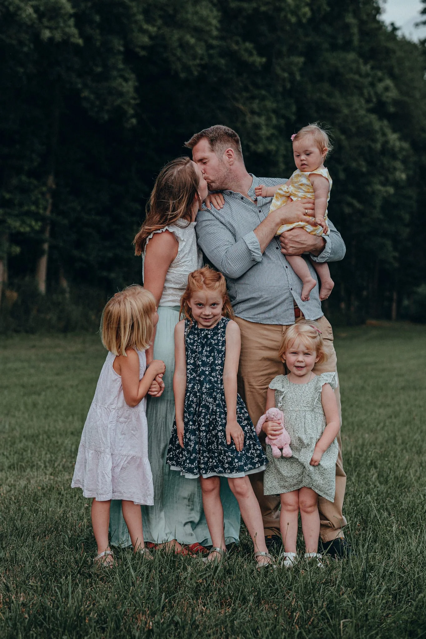 Familie mit Vater, Mutter und vier kleinen Mädchen, die im Grünen sitzen, beim Kuscheln und Kuss