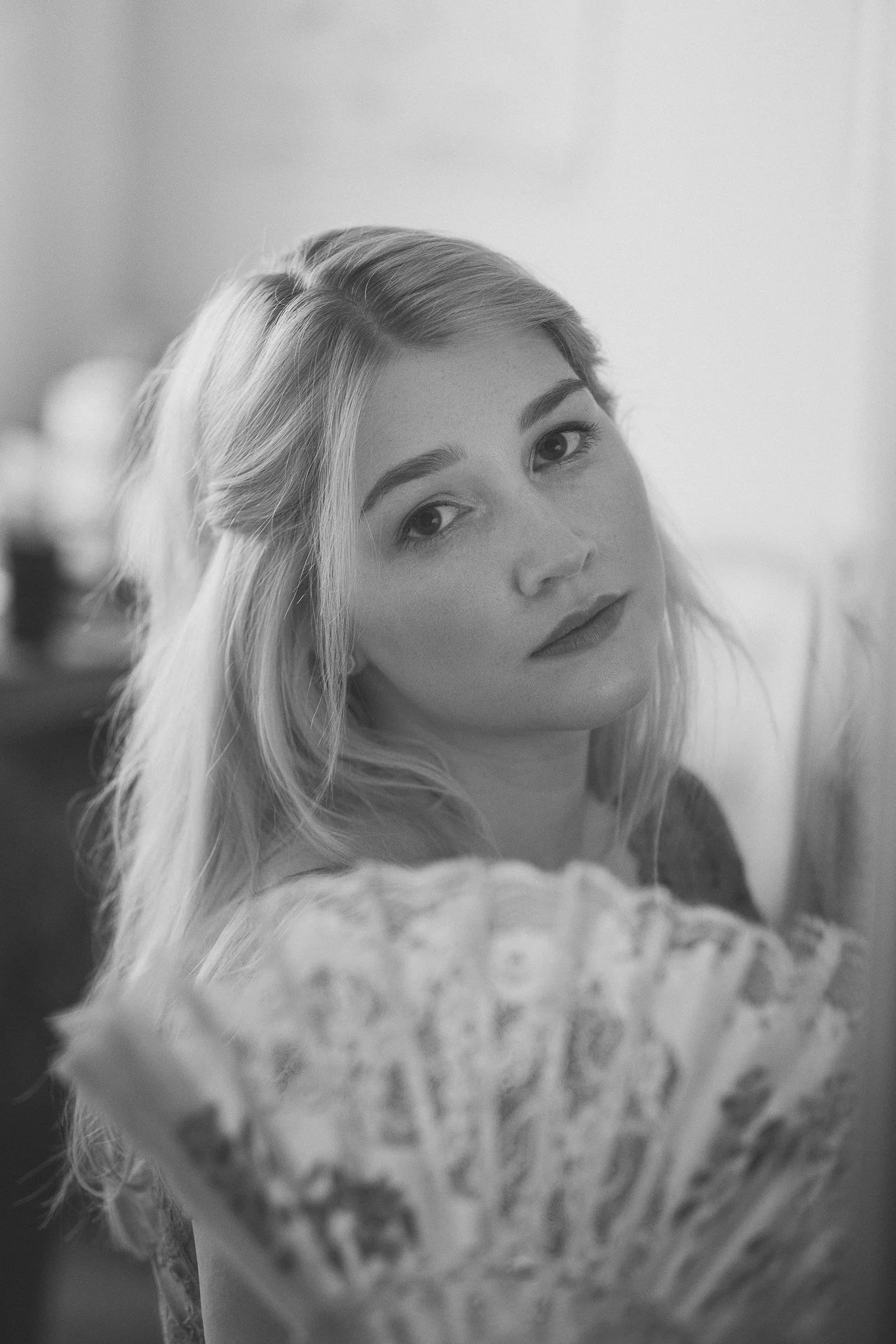 Schwarz-weiß-Foto eines jungen Mädchens mit langen Haaren, die in die Kamera schaut, während sie einen Fächer hält.