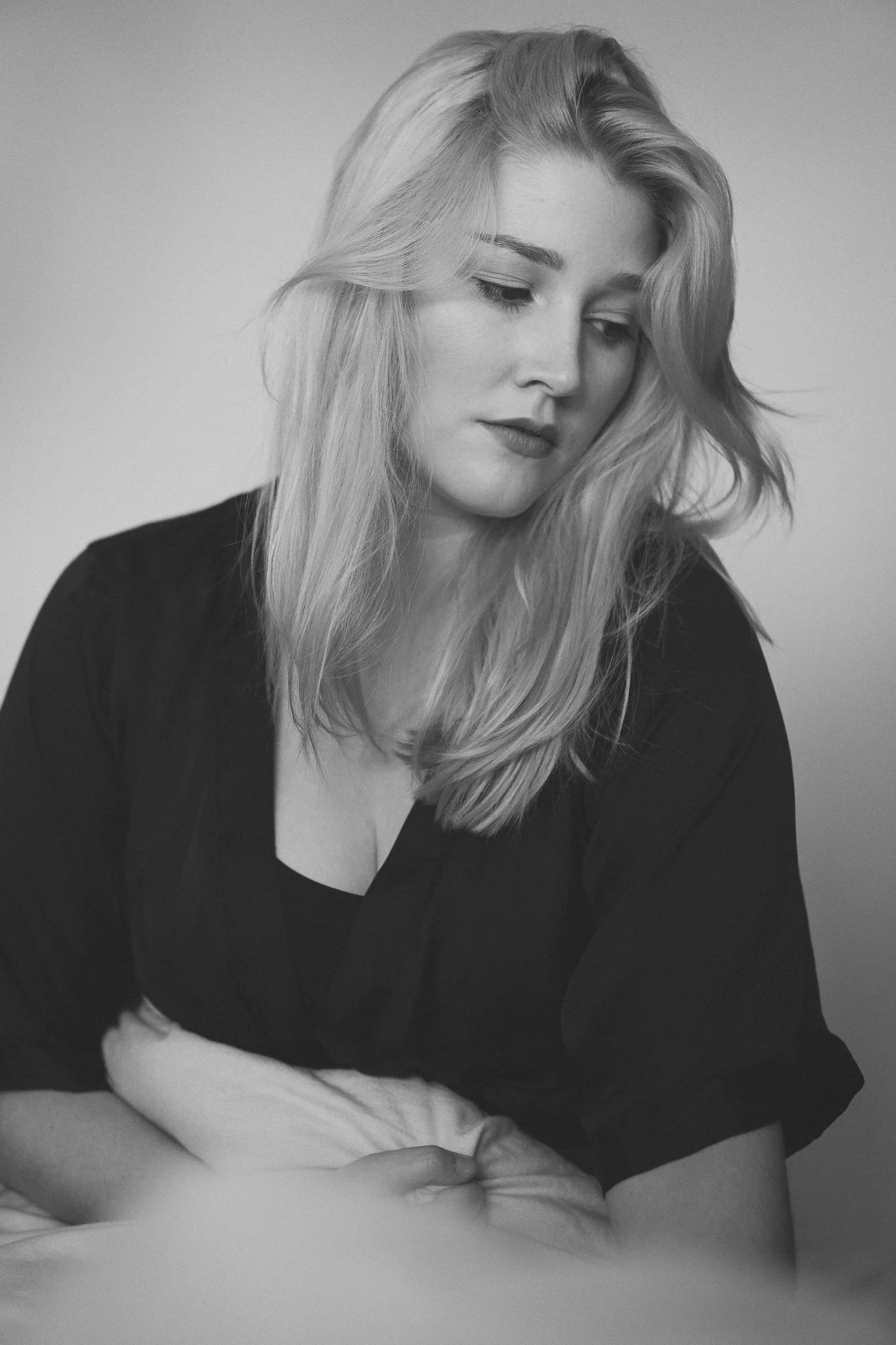 Schwarz-Weiß-Fotografie eines jungen Mädchens mit langen, gewellten blonden Haaren, das nach unten schaut, in einem dunkelfarbenen Oberteil.
