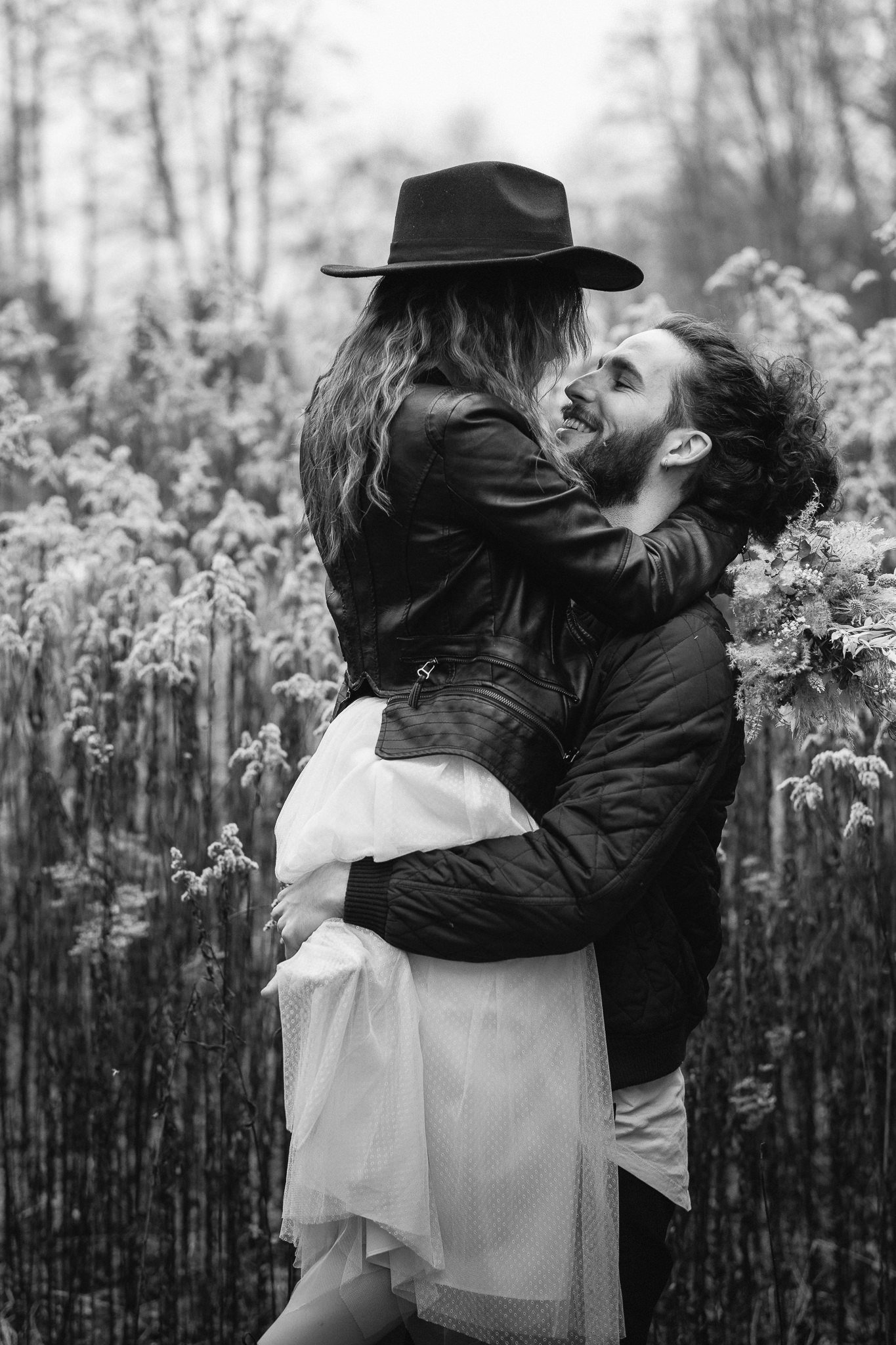 Ein Paar umarmt sich in einem Feld, die Frau hebt den Mann hoch. Es ist schwarz-weiß, das Paar lacht und blickt sich liebevoll an.