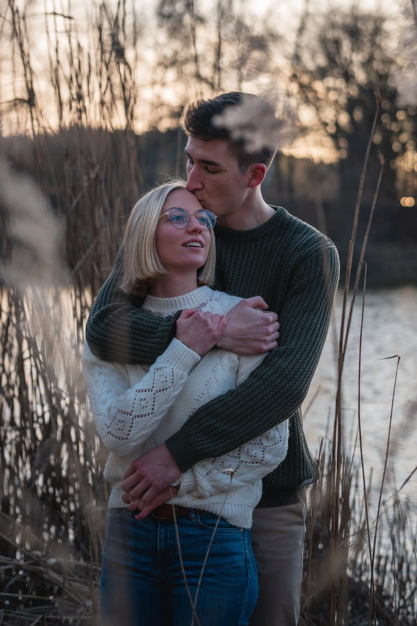 Ein Paar steht sich an einem Fluss bei Sonnenuntergang umarmend, mit dem Mann, der die Frau küsst.