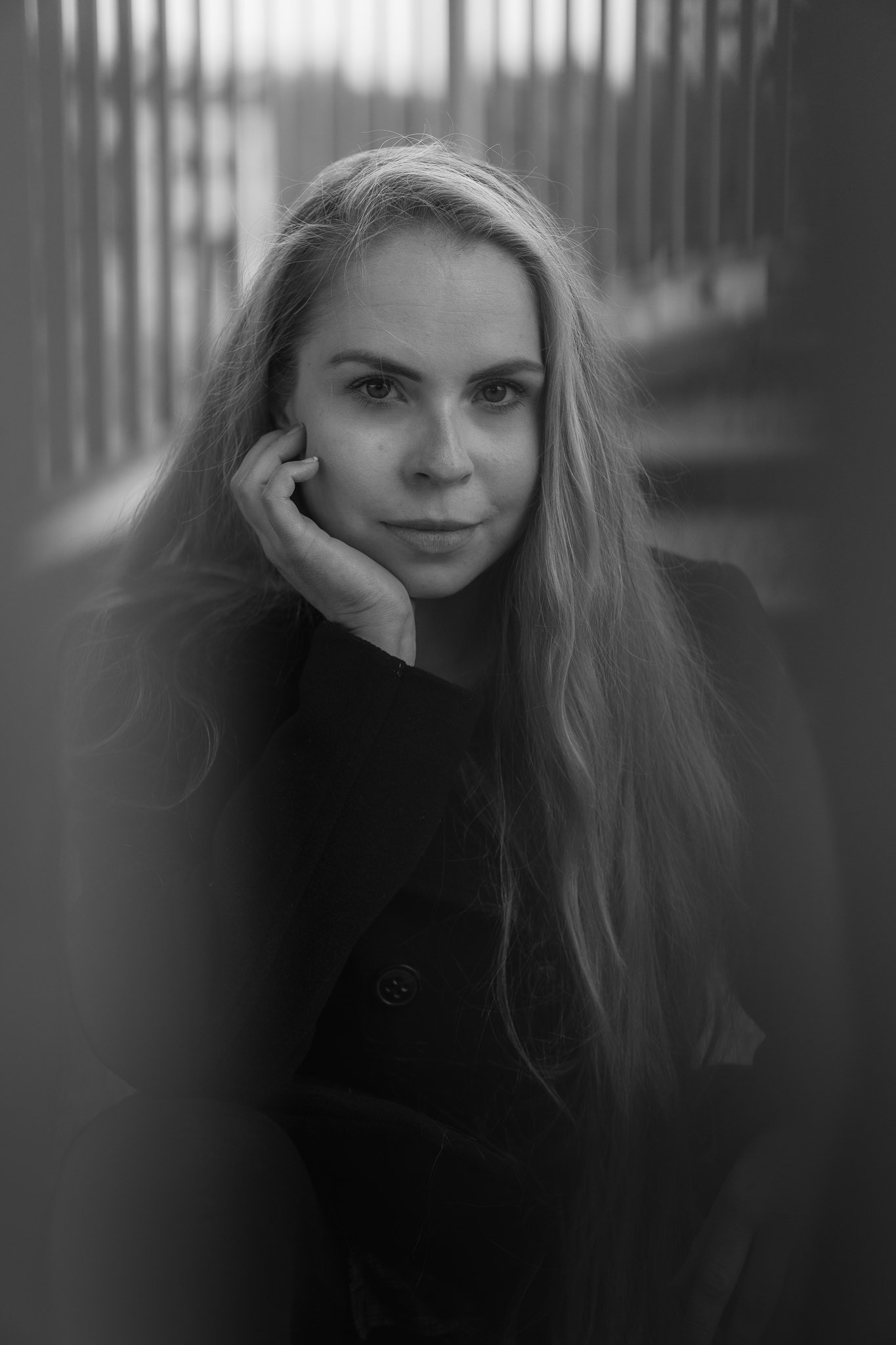 Schwarz-weiß-Fotografie eines jungen Mädchens mit langem Haar, das die Hand an das Gesicht legt, vor einem gelben Hintergrund mit vertikalen Linien.