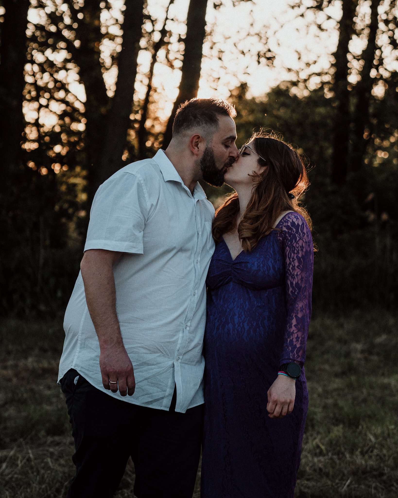 Ein Paar küsst sich bei Sonnenuntergang im Freien, im Hintergrund Bäume.