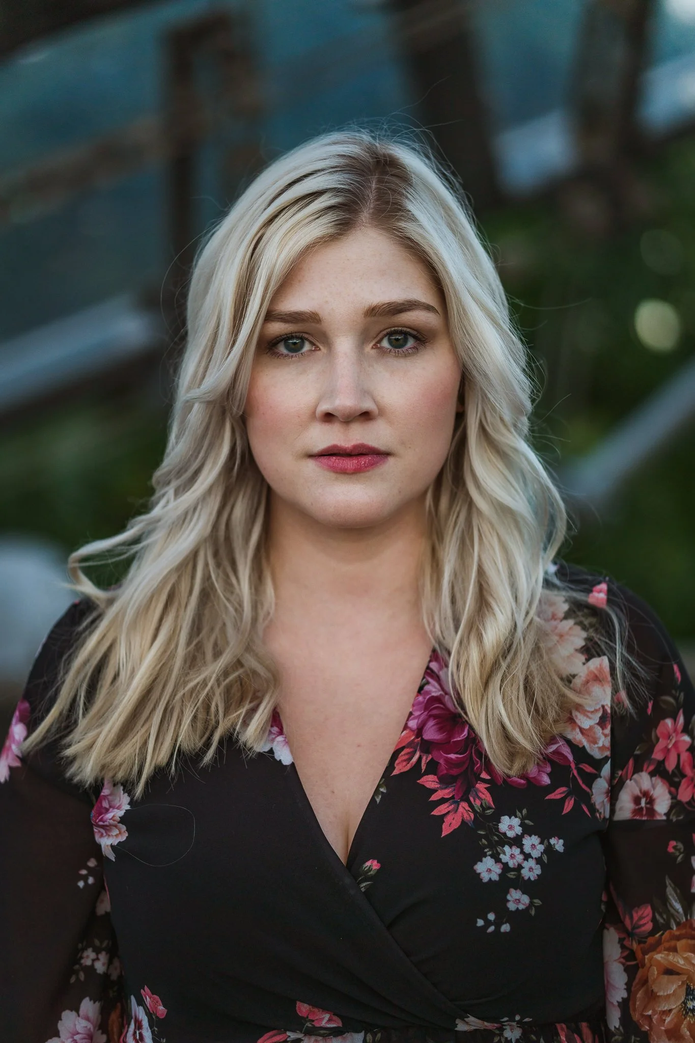 Nahaufnahme einer jungen Frau mit blonden, gewellten Haaren vor einem unscharfen Hintergrund im Freien.