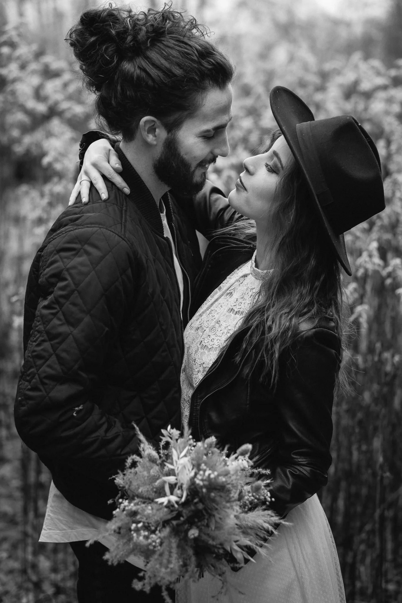 Ein verliebtes Paar steht im Freien, die Frau hält einen Blumenstrauß, beide schauen sich verliebt an, die Frau trägt einen Hut, das Bild ist in Schwarz-Weiß.