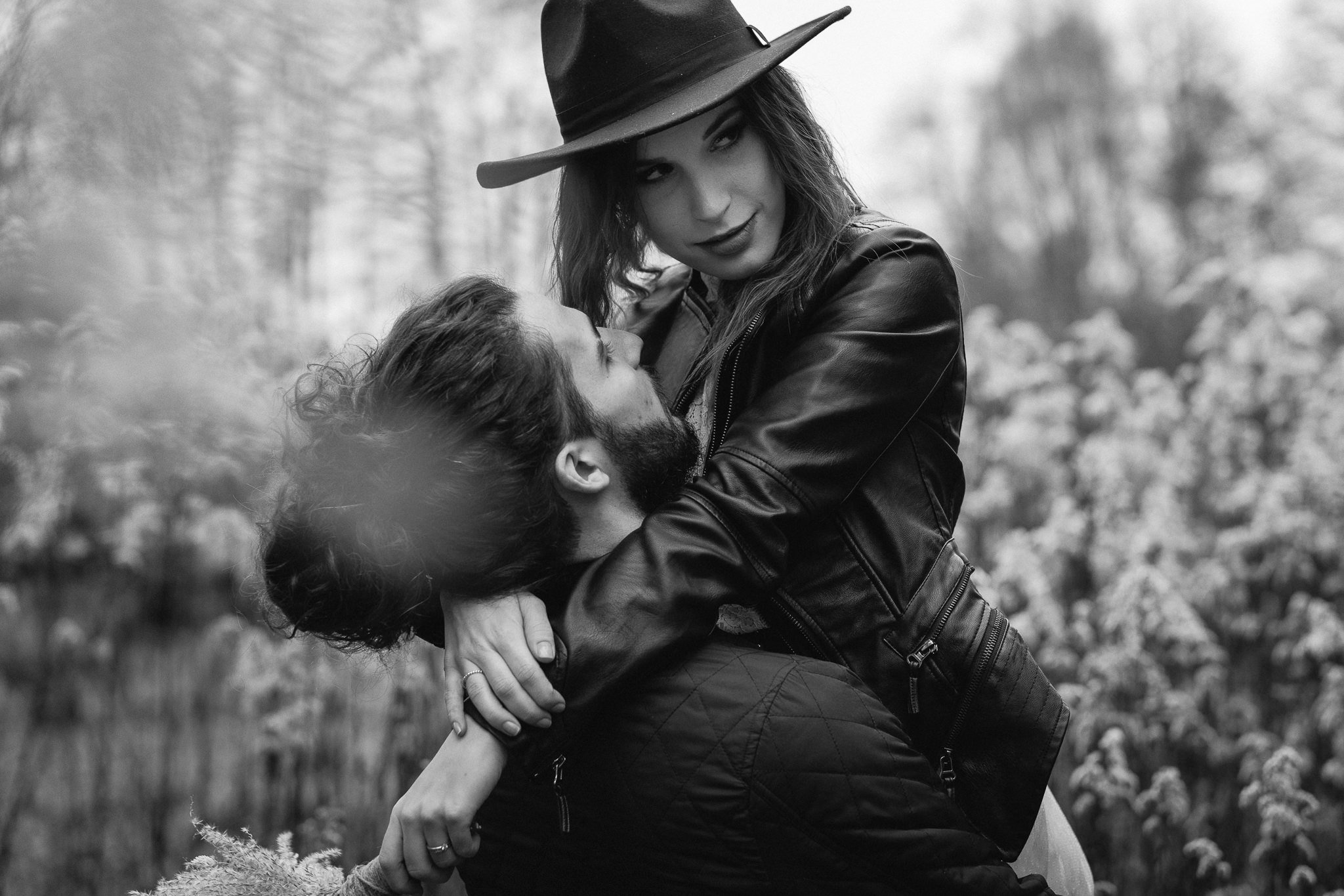 Schwarz-Weiß-Foto eines Paares im Freien, die Frau trägt einen Hut und eine Lederjacke, der Mann hat einen Bart. Sie umarmen sich liebevoll.