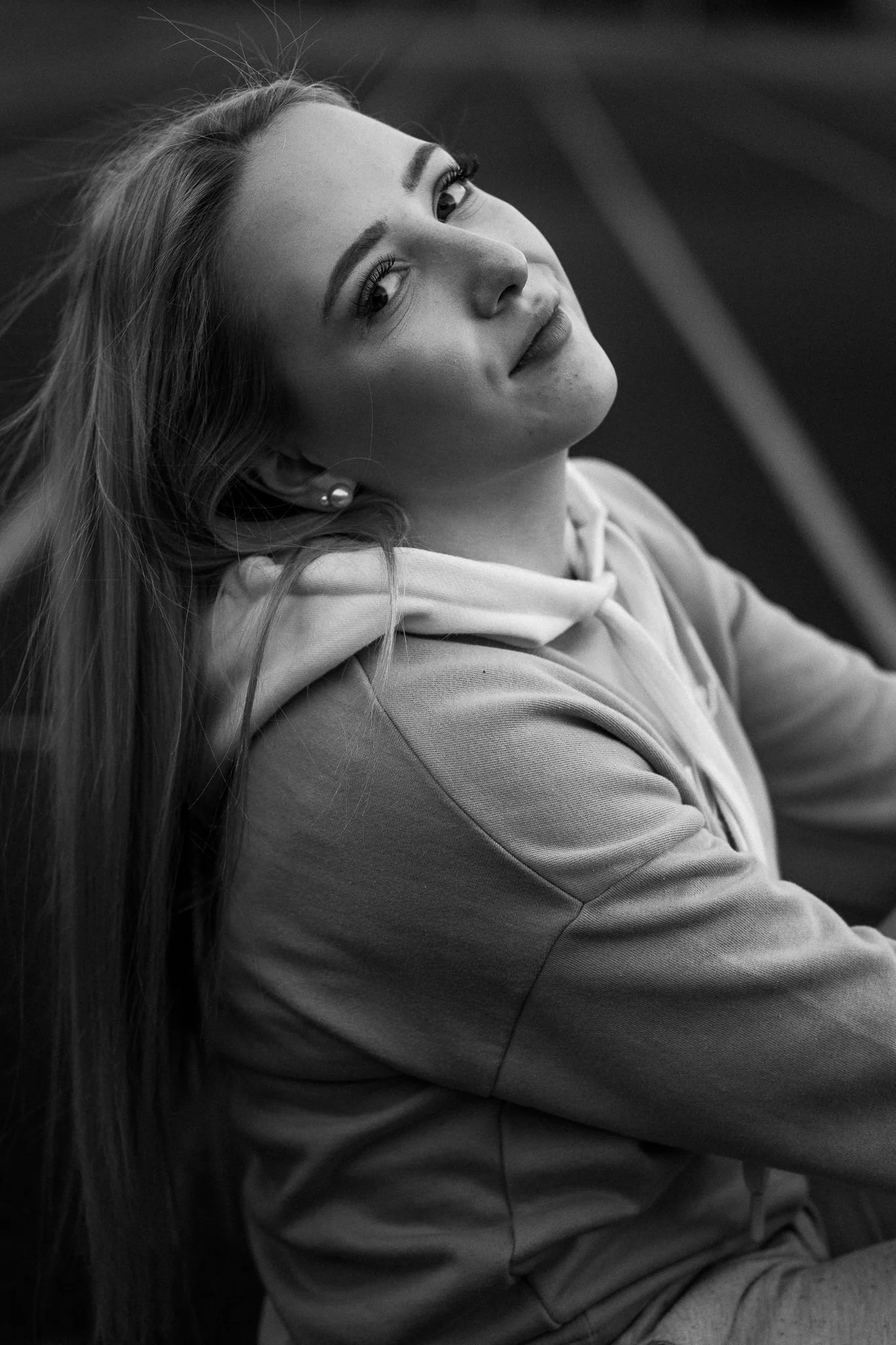 Schwarz-Weiß-Fotografie eines jungen Mädchens mit langen Haaren, die eine Jacke trägt und leicht lächelt, Blick leicht nach oben gerichtet.