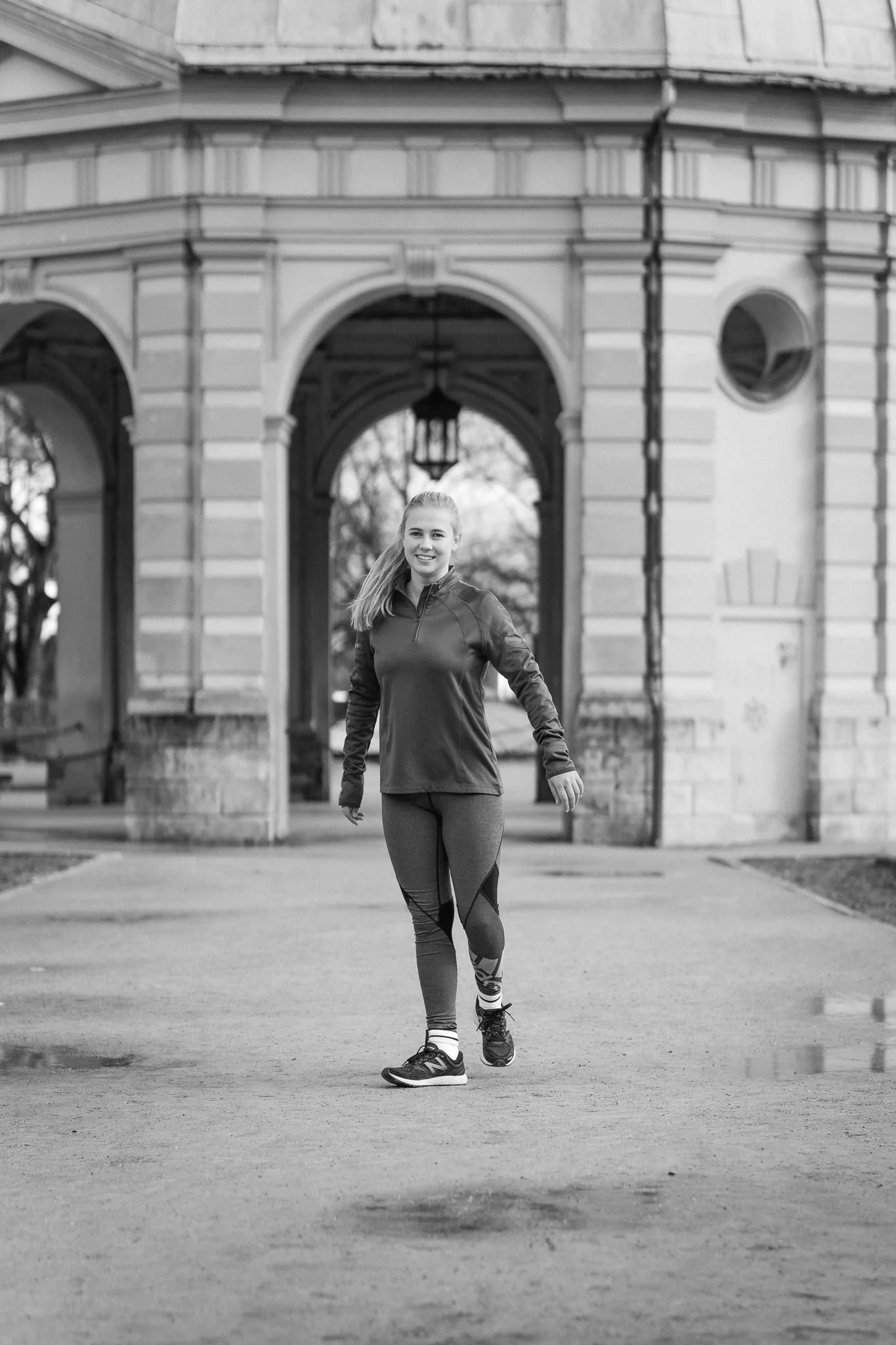 Junge Frau joggt vor einem historischen Gebäude mit Arkaden und Laterne, schwarz-weiß Fotografie