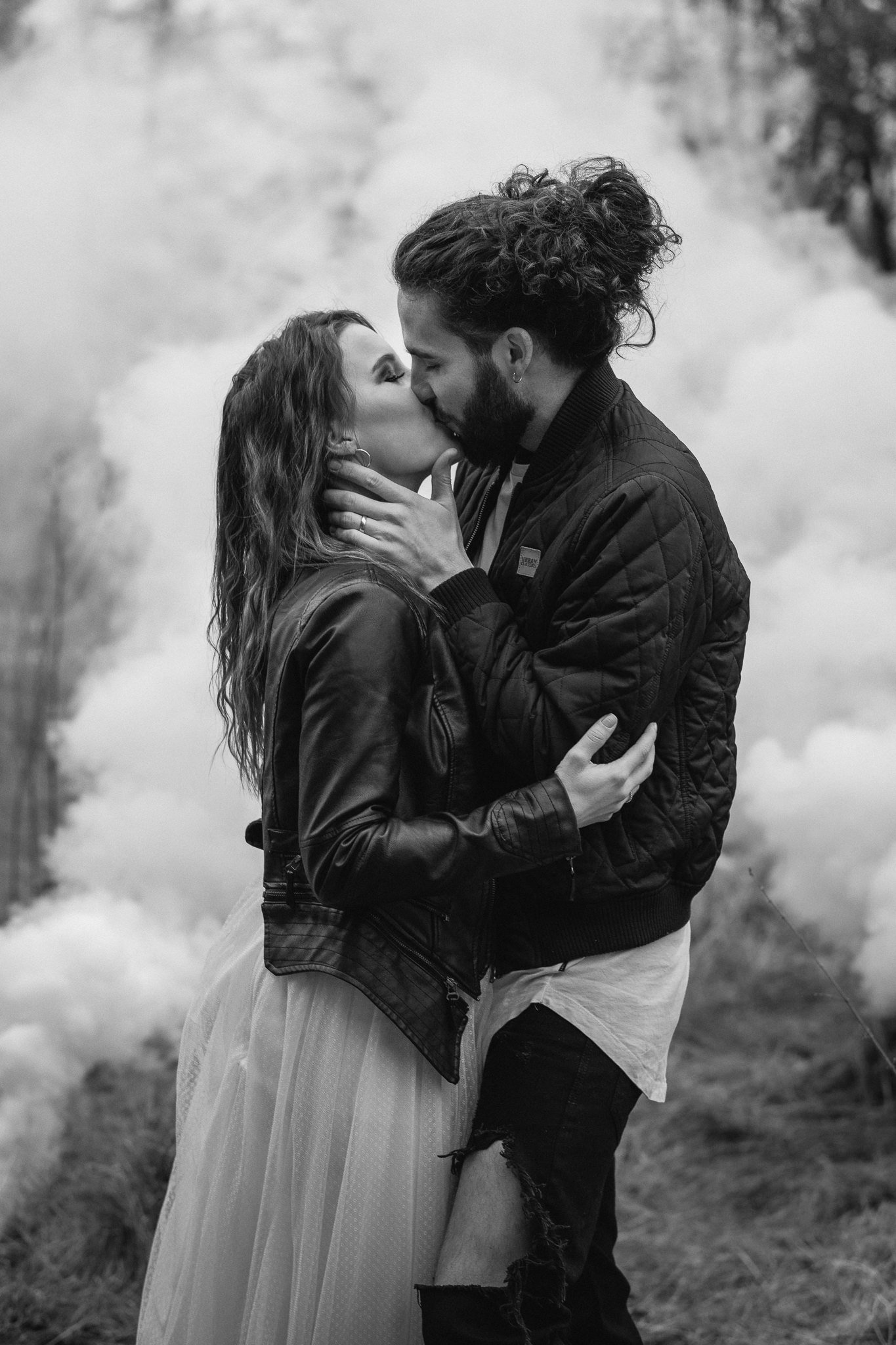 Ein verliebtes Paar umarmt sich und küsst sich in einer nebeligen, natürlichen Umgebung, schwarz-weiß aufgenommen.