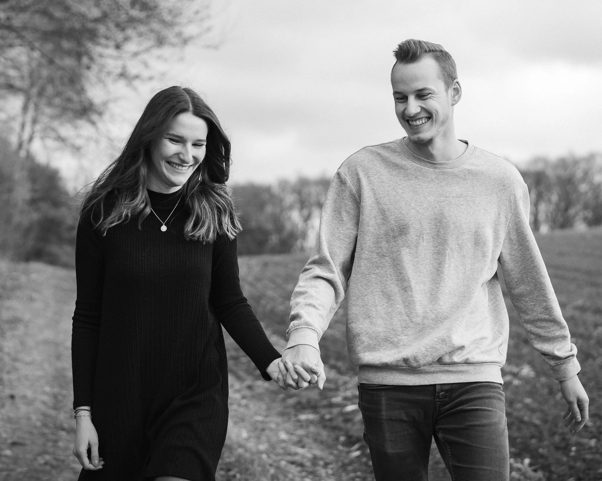 Ein Mann und eine Frau gehen Händchen haltend im Freien, beide lächeln.