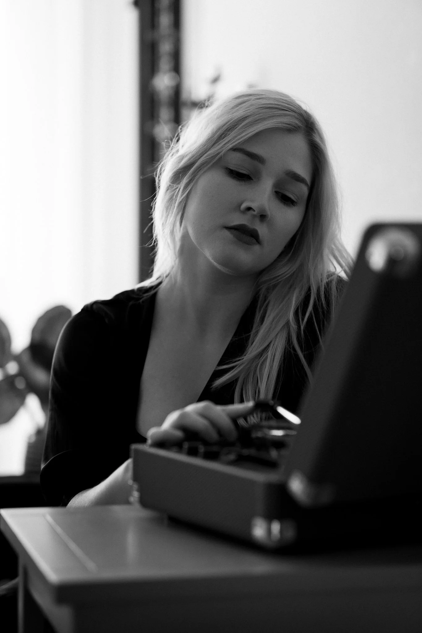 Eine junge Frau mit langen, hellen Haaren arbeitet an einem Laptop in einem Raum, der vermutlich eine Café oder ein Arbeitsplatz ist.