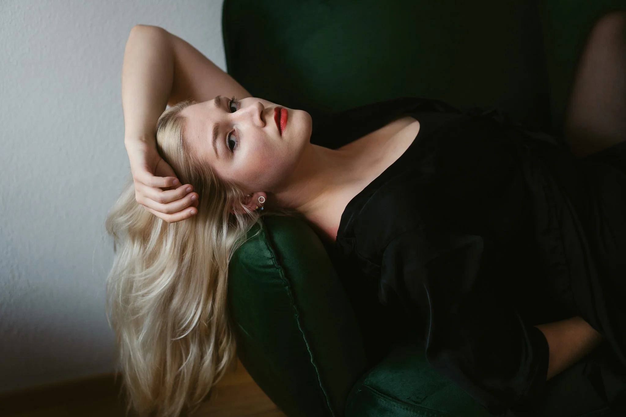 Junge Frau mit blonden Haaren, rote Lippen, schwarze Kleidung, liegt auf einem grünen Stuhl, Blick nach oben, entspannt.